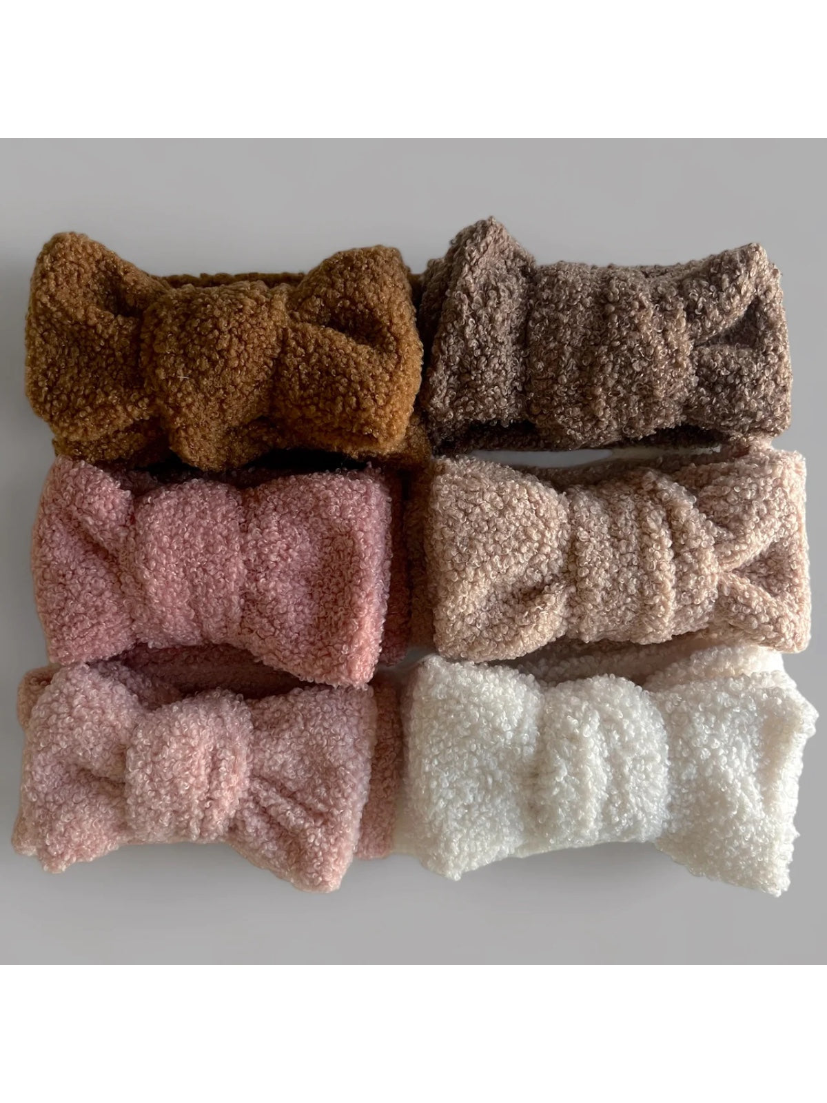 Six soft, plush headbands in shades of brown, pink, and white arranged in a row on a light background.