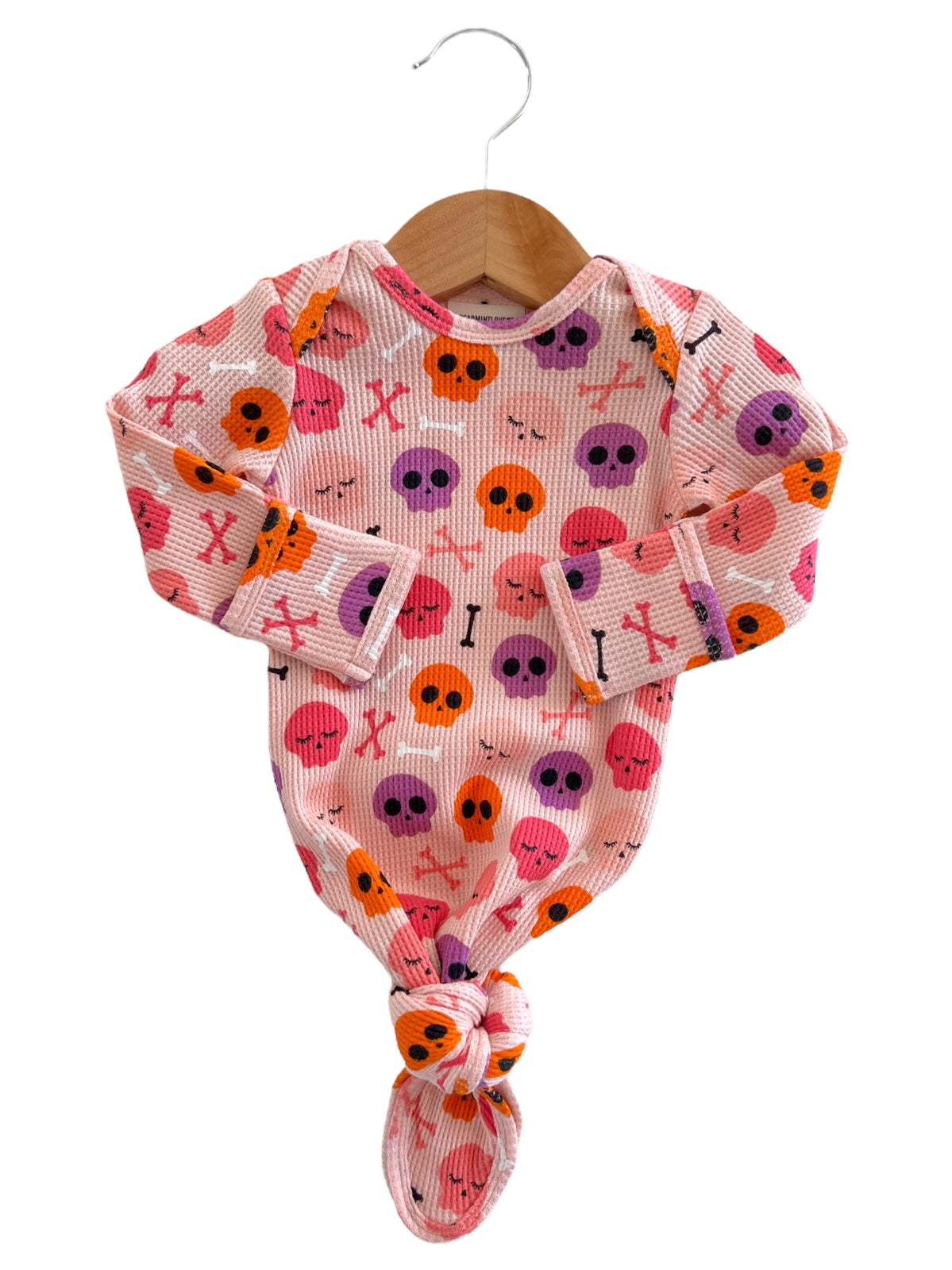 Baby onesie with colorful skull and bone print, hanging on a wooden hanger against a white background.