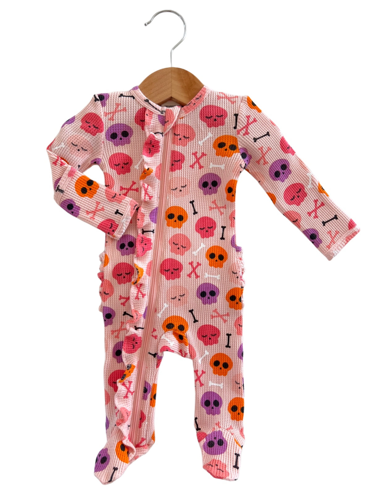 Pink children's pajamas with skull and crossbones pattern, hanging on a wooden hanger.