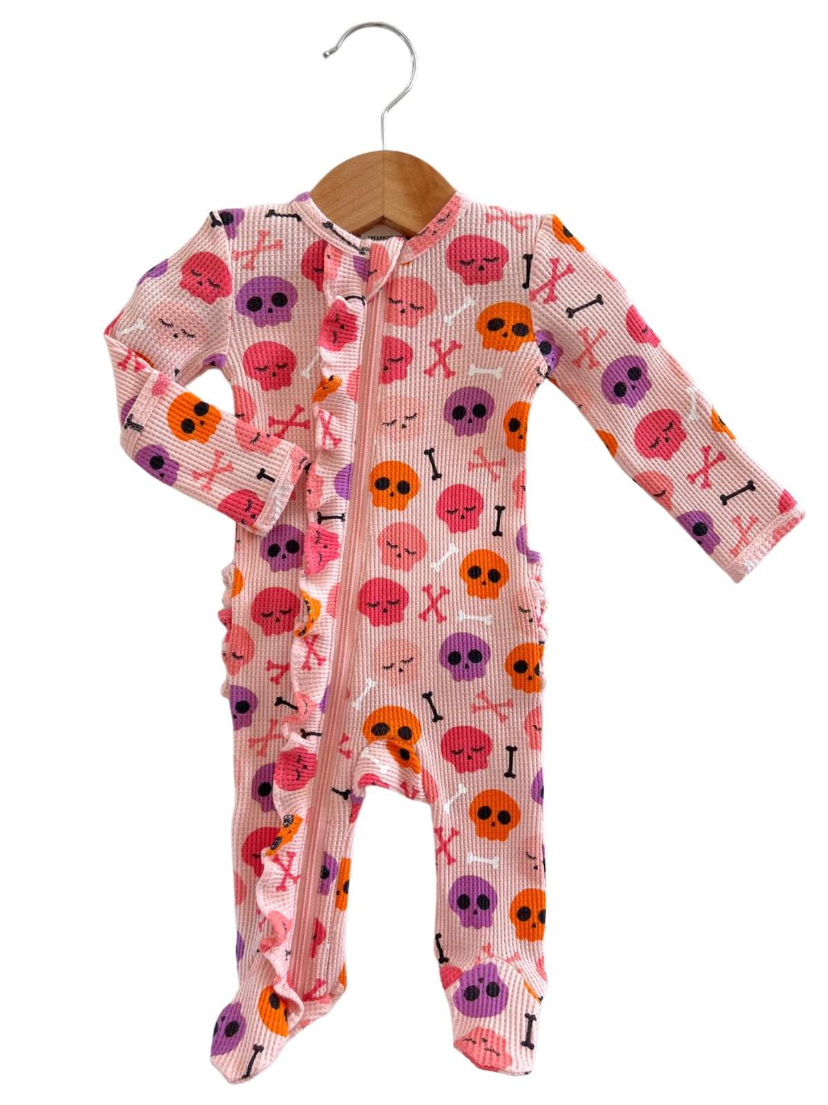 Pink children's pajamas with skull and crossbones pattern, hanging on a wooden hanger.