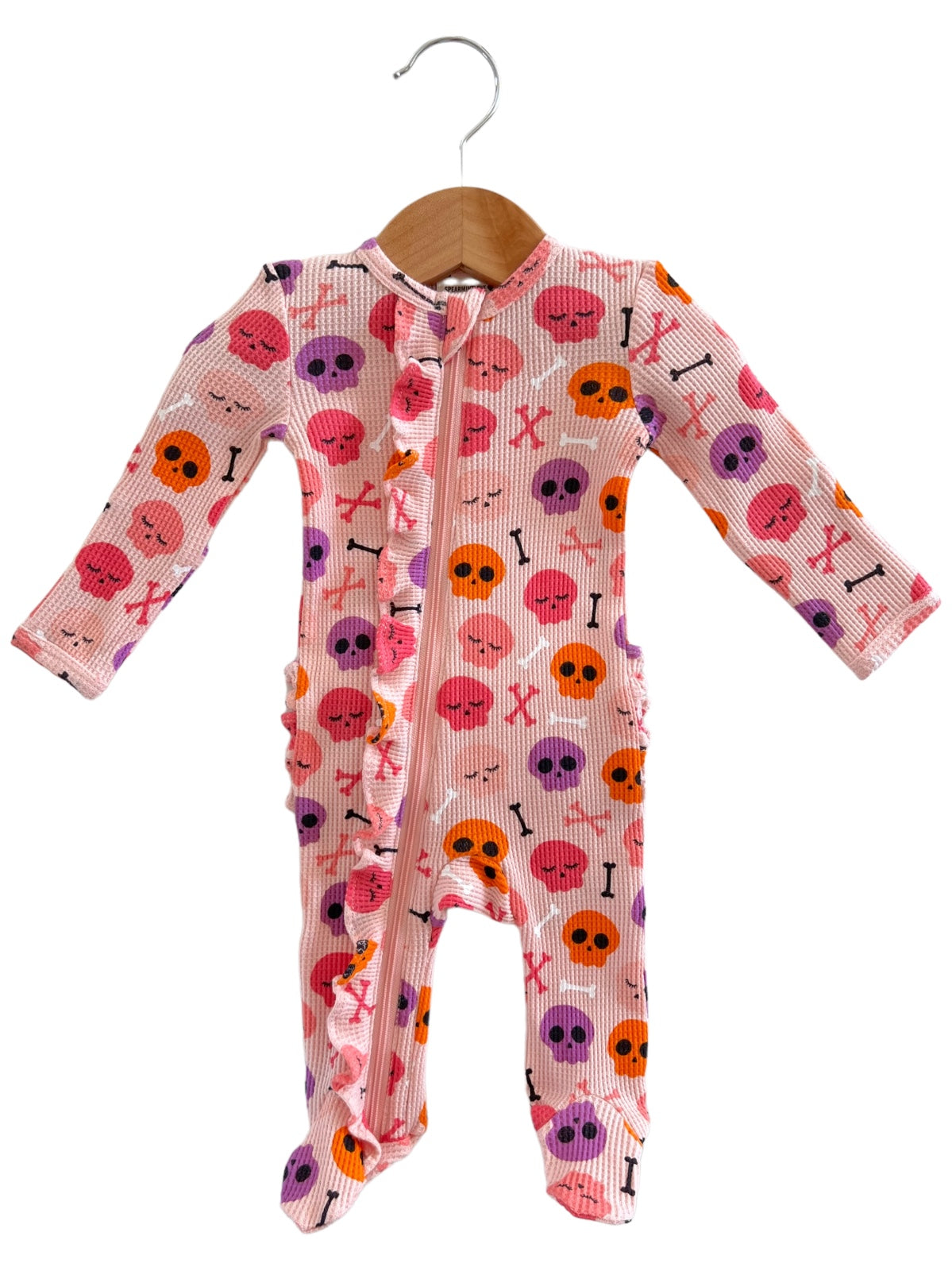 Pink baby onesie with skull and crossbones pattern hanging on a wooden hanger.