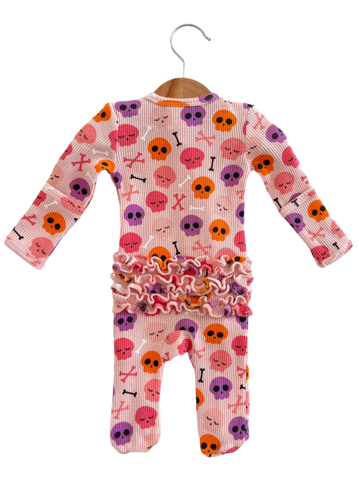 Pink baby onesie with skull and crossbones pattern, accented with ruffled trim at the waist.