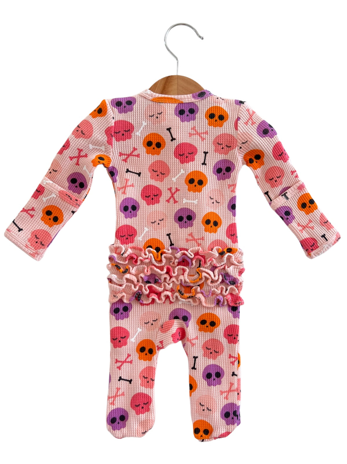 Pink baby onesie with skull and crossbones pattern, accented with ruffled trim at the waist.