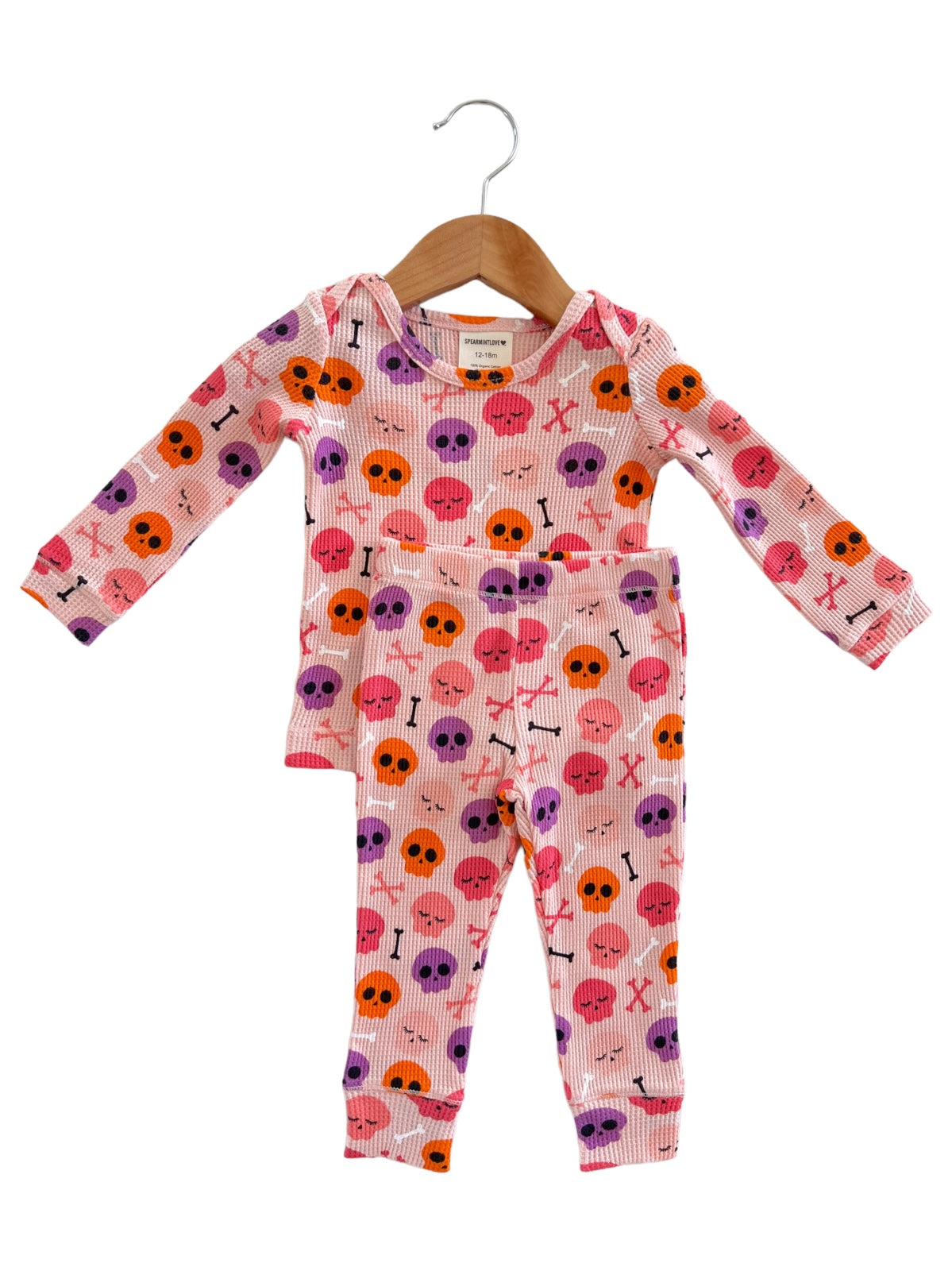 Children's pajamas featuring colorful skull and crossbone patterns, hung on a wooden hanger.