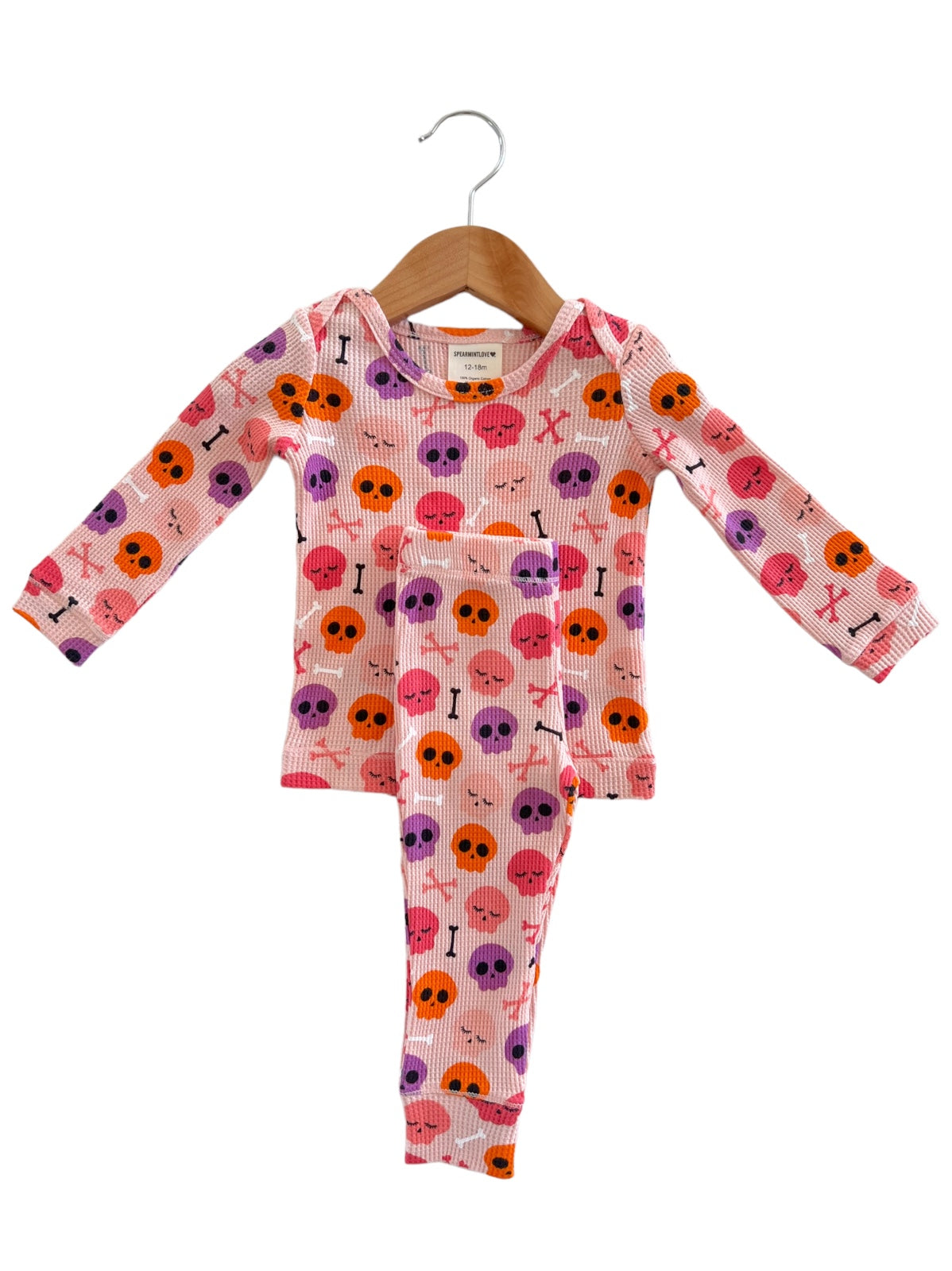 Pink toddler pajamas with colorful skull and bone patterns, hanging on a wooden hanger.