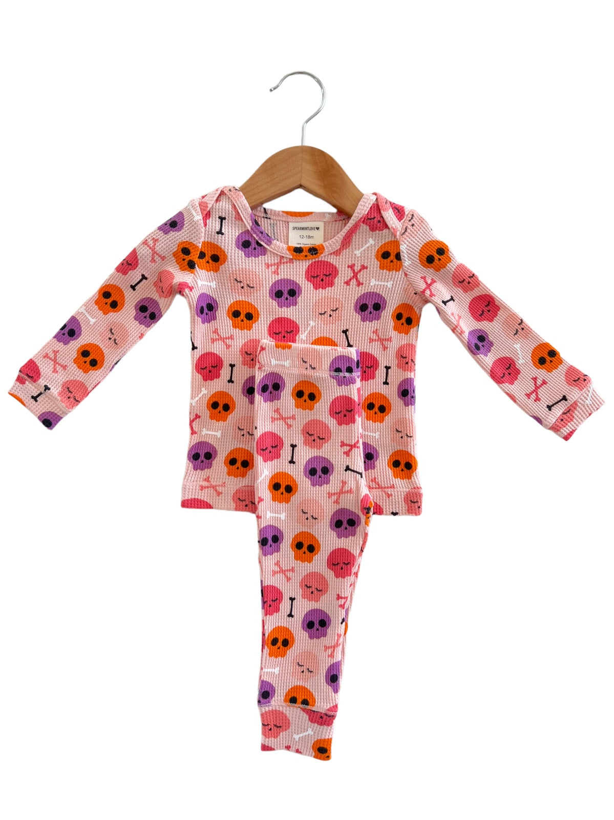 Pink toddler pajamas with colorful skull and bone patterns, hanging on a wooden hanger.