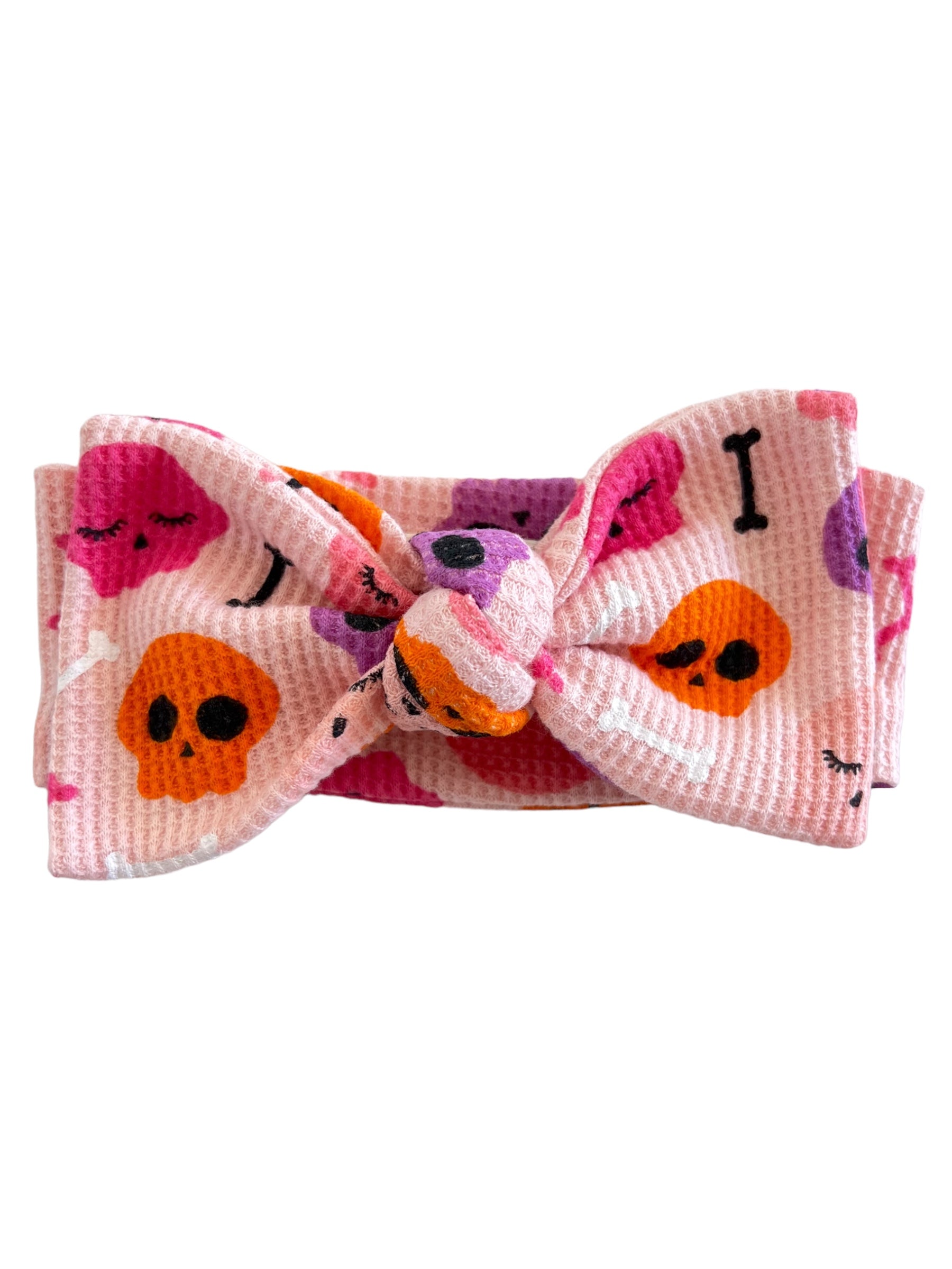 Pink fabric headband with skull and crossbone patterns tied in a bow.