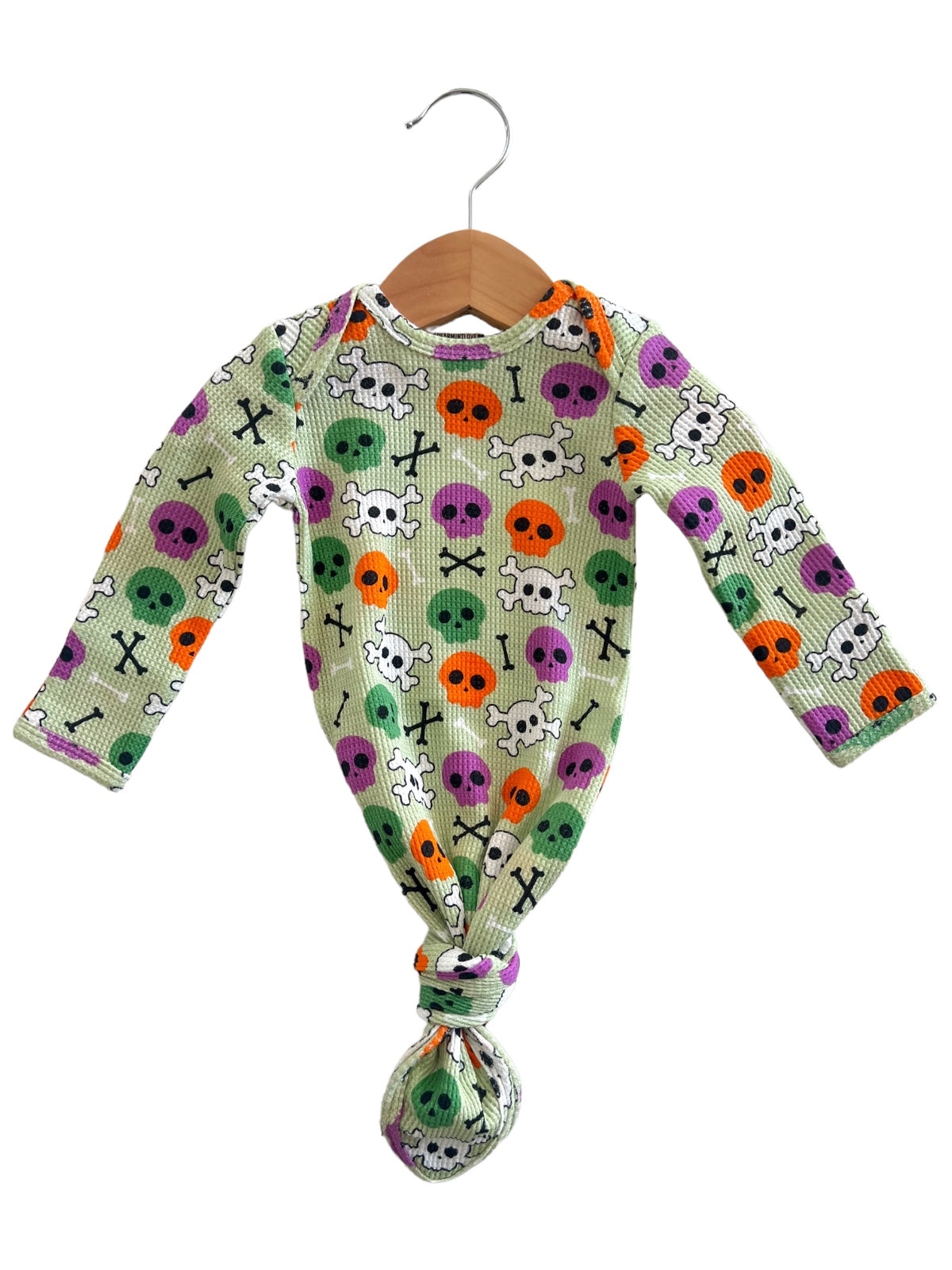 Green baby outfit with colorful skull and crossbones pattern, hanging on a wooden hanger.