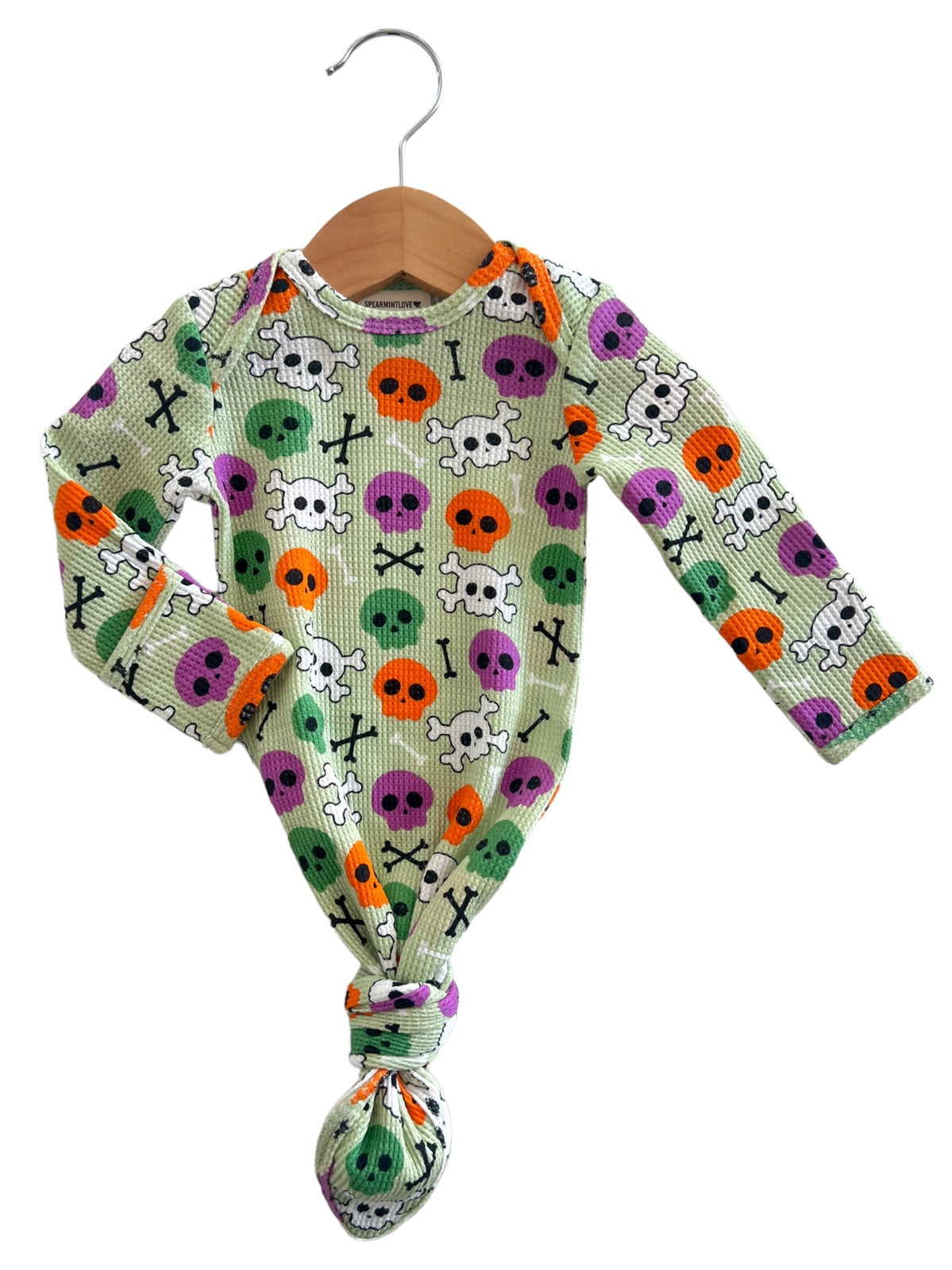 Long-sleeve baby onesie with colorful skull and crossbones print, hanging on a wooden hanger.