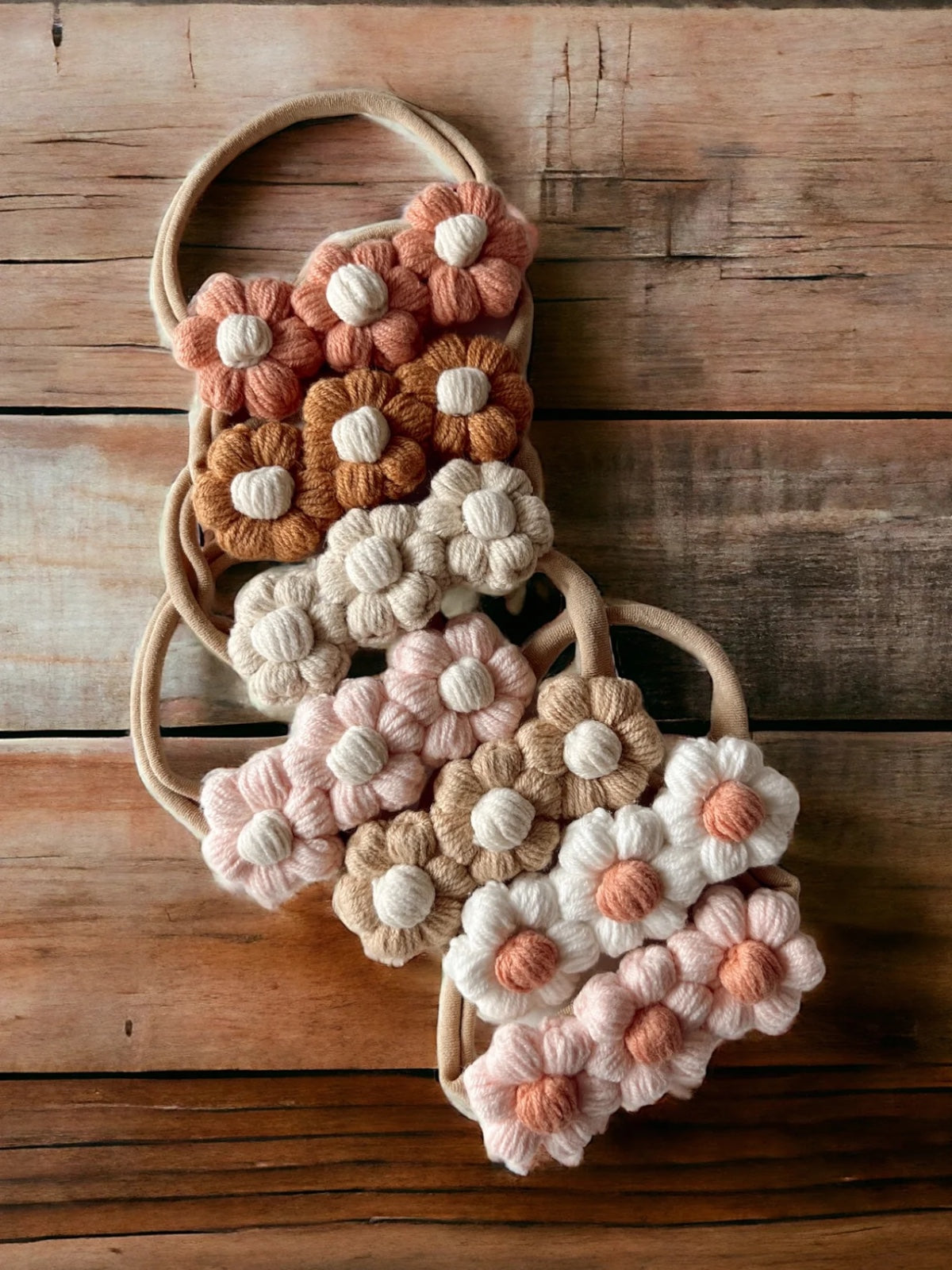 Colorful knitted flower hair ties arranged on a wooden surface.