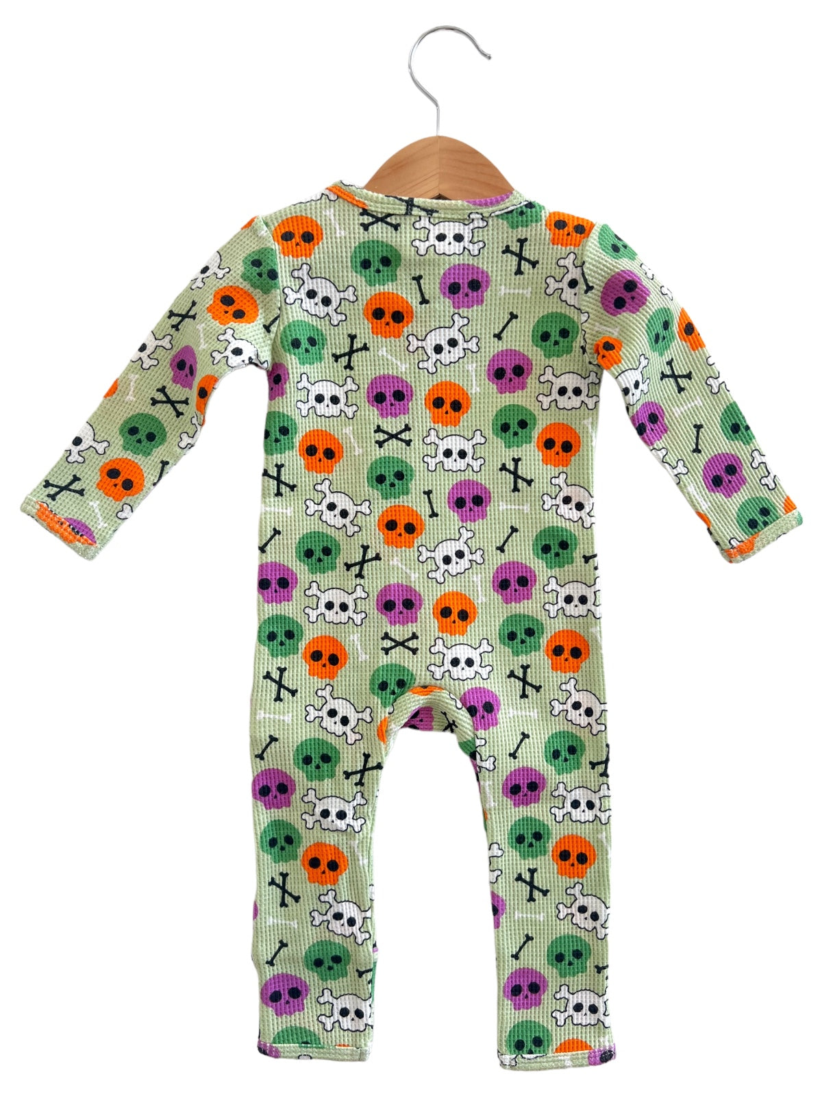 Colorful kids' onesie featuring skull and crossbones pattern in various hues on a light green background.