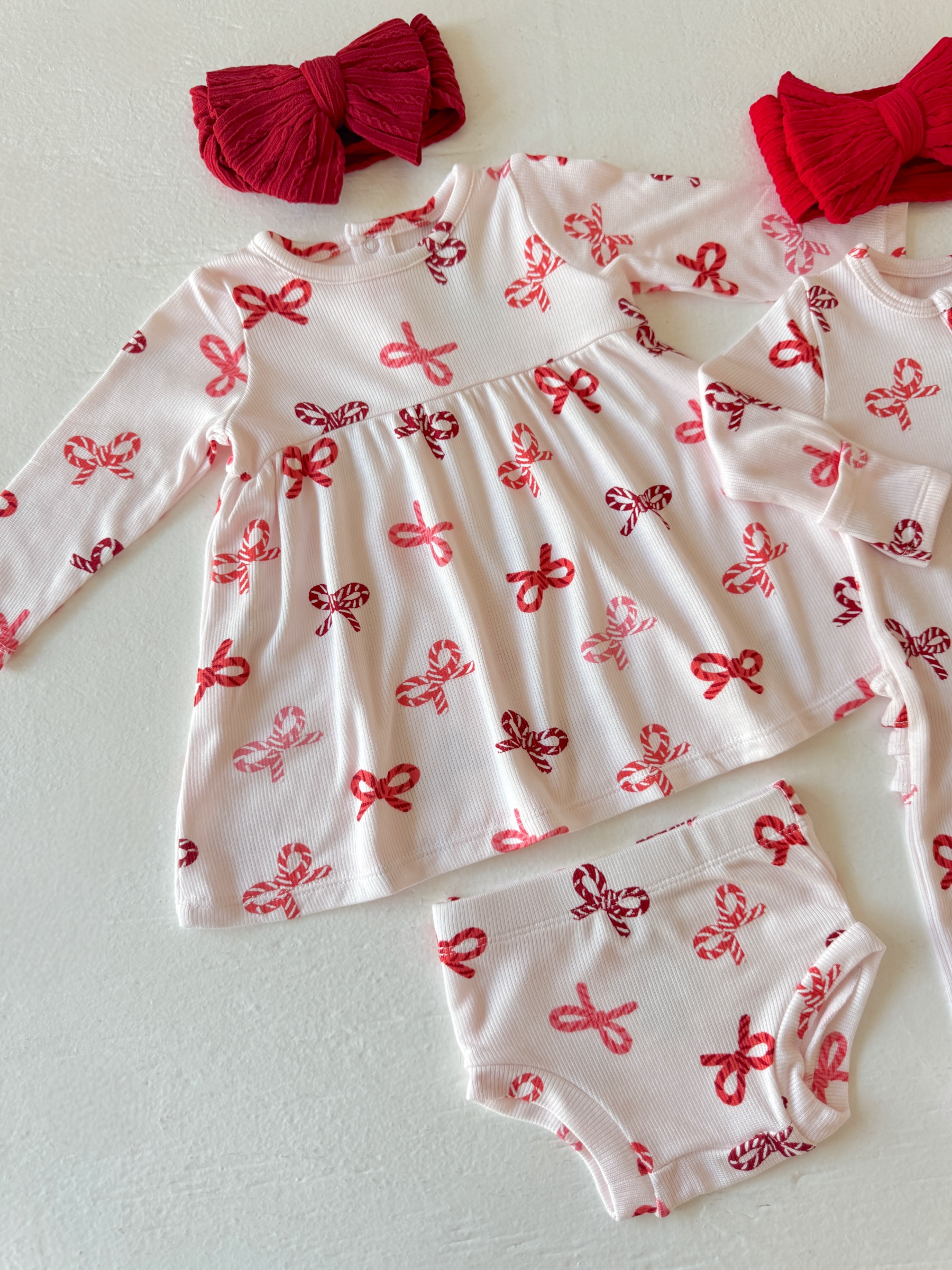 Cute toddler outfit featuring a dress with candy-striped bows and coordinating bloomers, alongside red hair bows.
