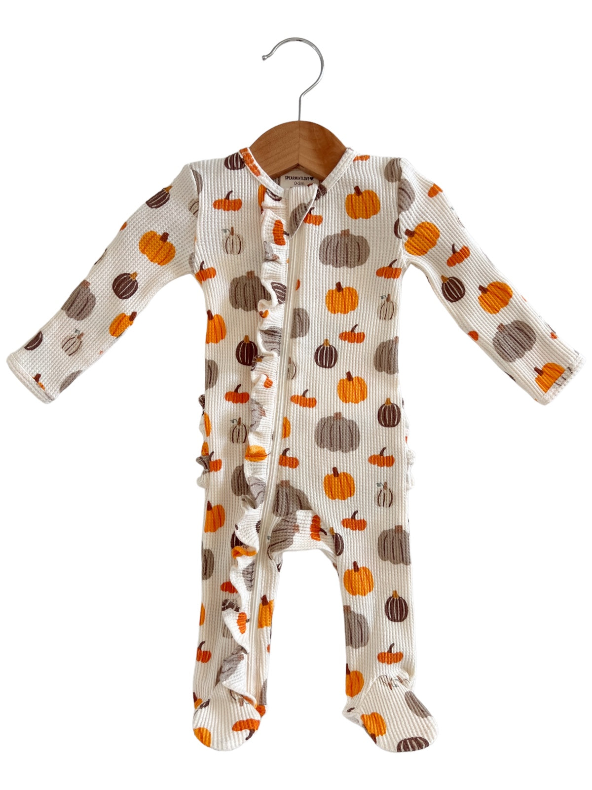 Baby onesie with a pumpkin print, featuring long sleeves and a ruffled front, hanging on a wooden hanger.
