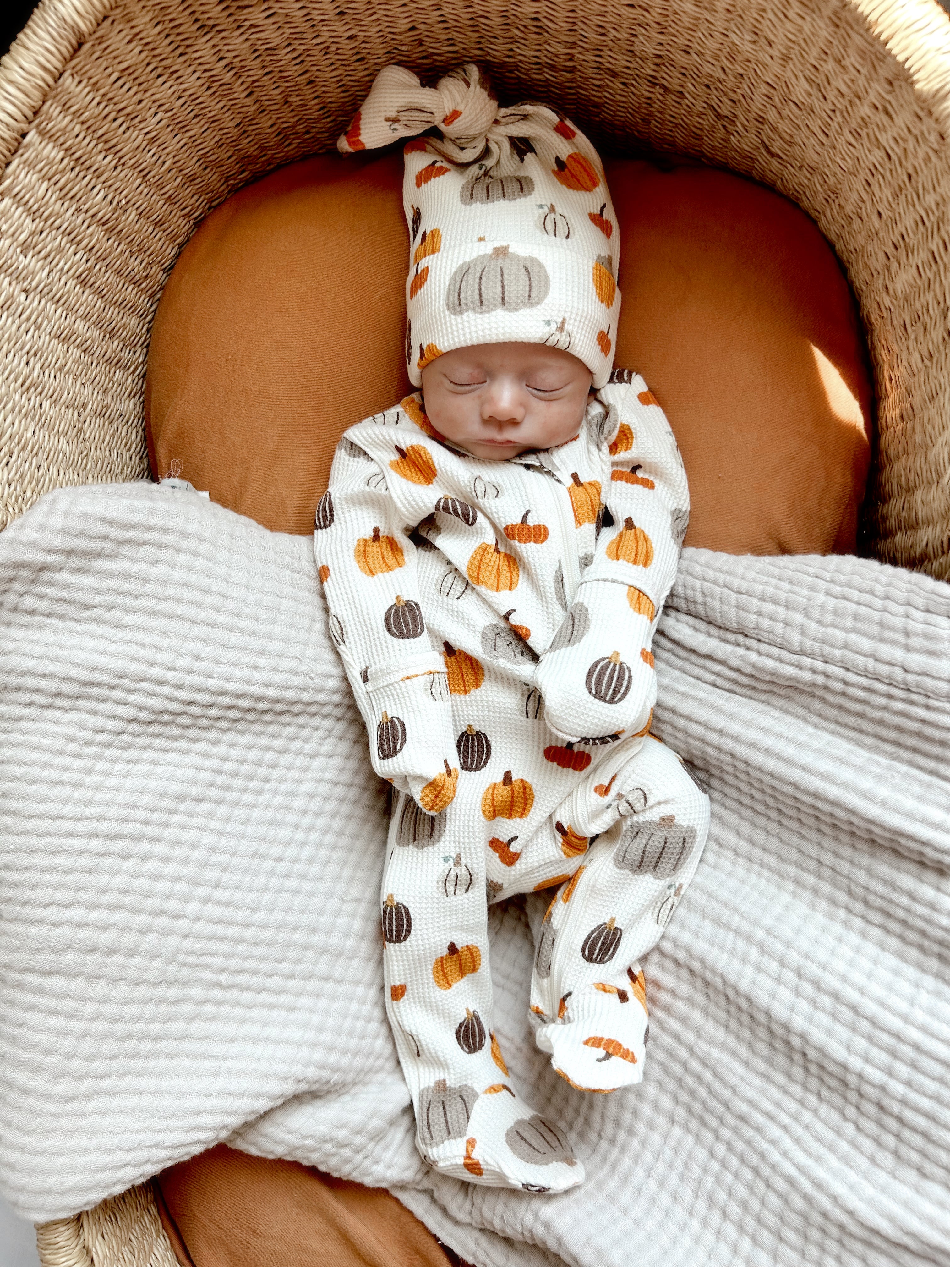 Baby dressed in pumpkin-themed outfit and hat, resting peacefully in a woven basket on a soft blanket.