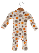 Infant onesie with a pumpkin print in orange and brown shades, hanging on a wooden hanger.