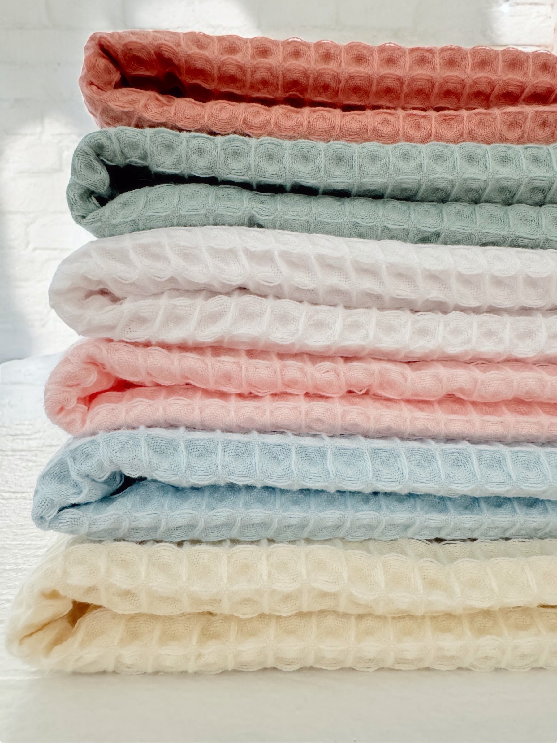 Stack of textured fabric blankets in soft pastel colors: pink, green, white, blue, and cream.
