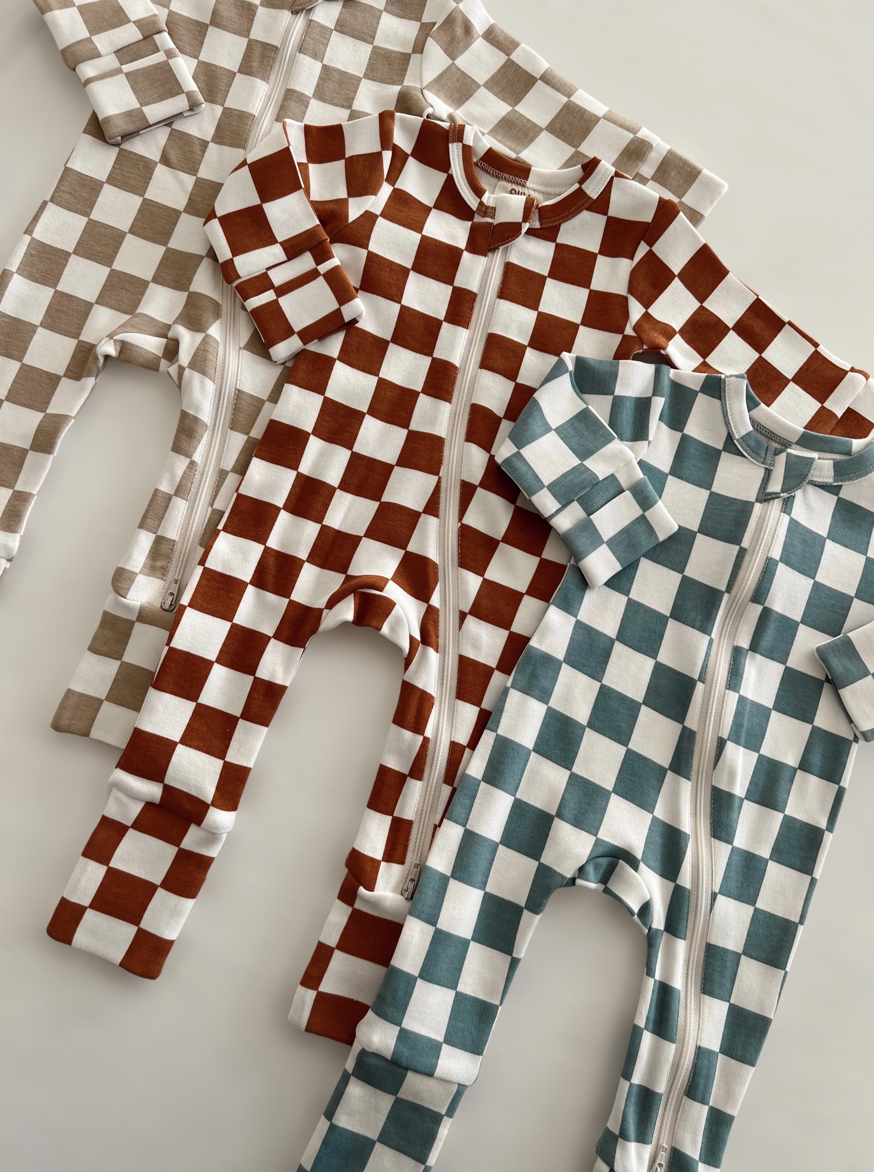 Three checkered baby onesies in brown, blue, and beige laid flat on a light background.