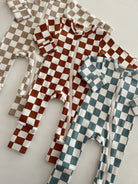 Three checkered baby onesies in brown, blue, and beige laid flat on a light background.