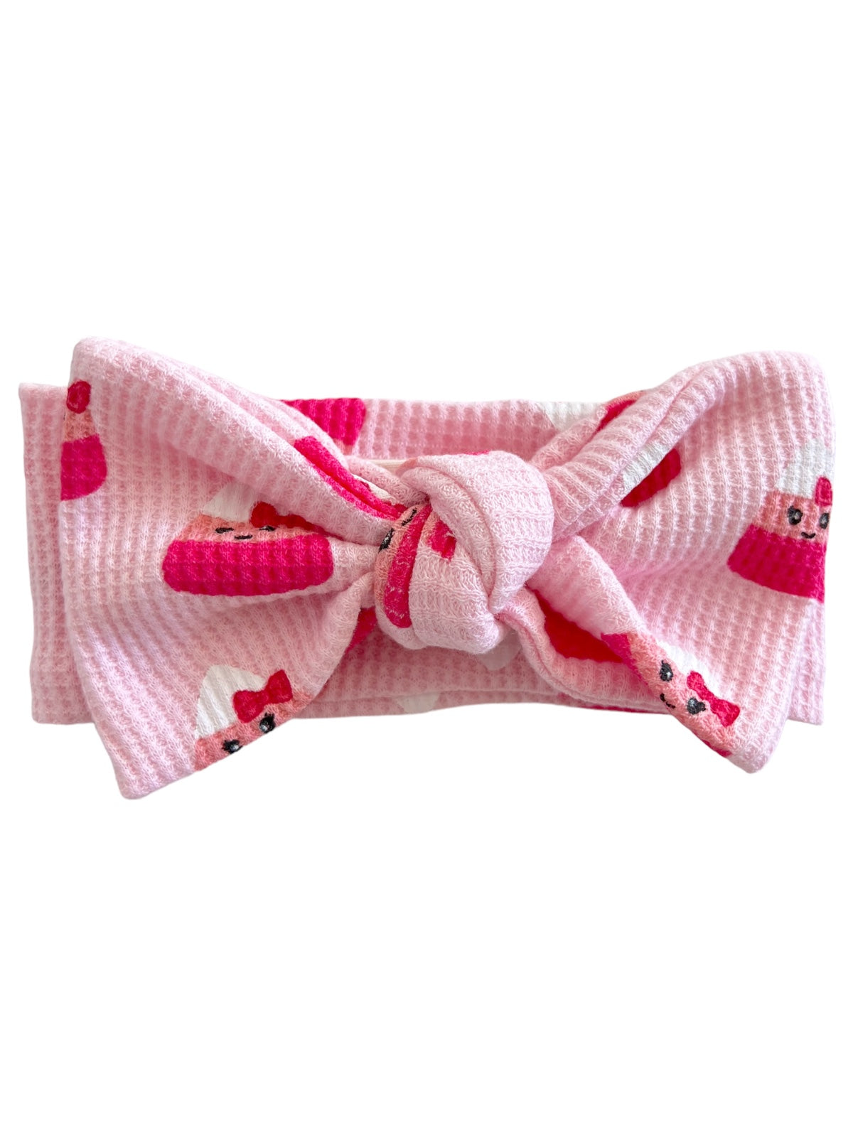 Pink fabric headband with bow, featuring a whimsical cupcake pattern. Ideal for casual or festive outfits.