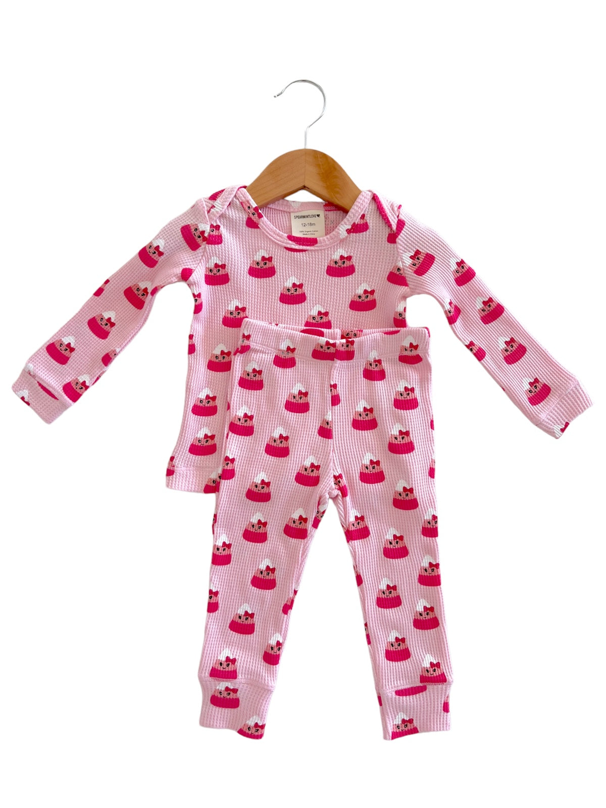 Children's pink pajamas with cupcake pattern, featuring a long-sleeve top and matching pants, displayed on a hanger.