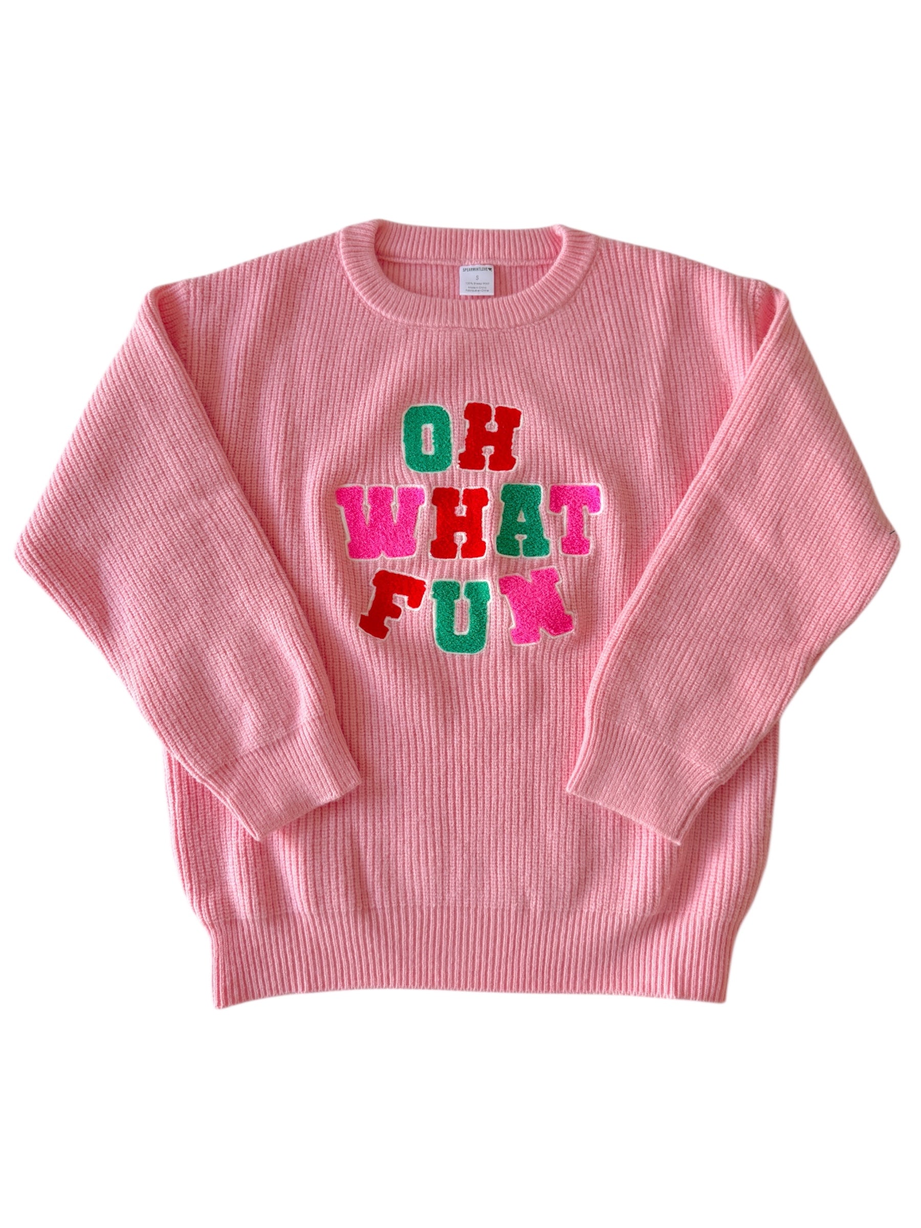 Pink sweater with colorful text "OH WHAT FUN" in bold letters across the front. Cozy and festive style.