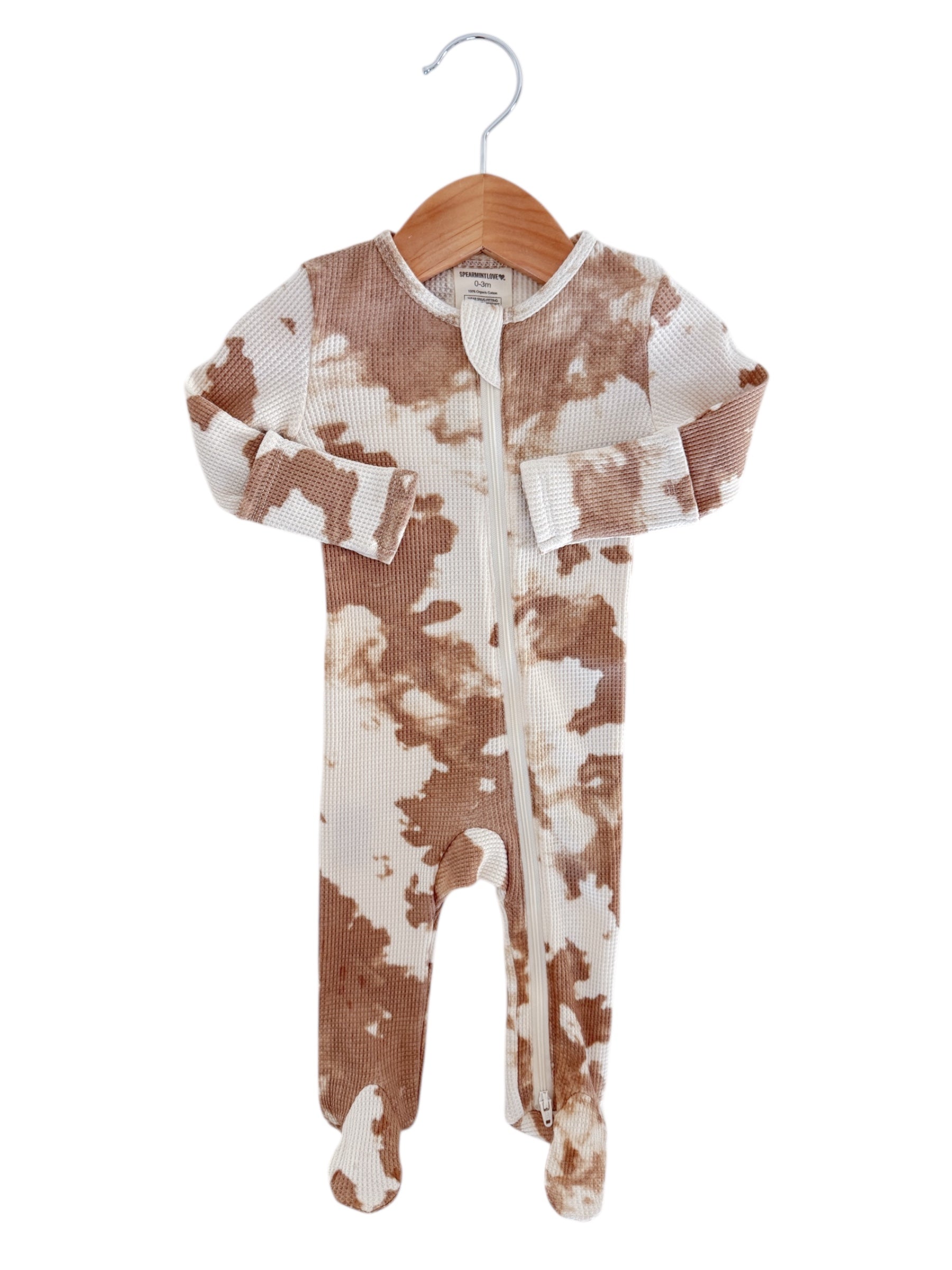 Tan and white baby onesie with long sleeves and feet, displayed on a wooden hanger.