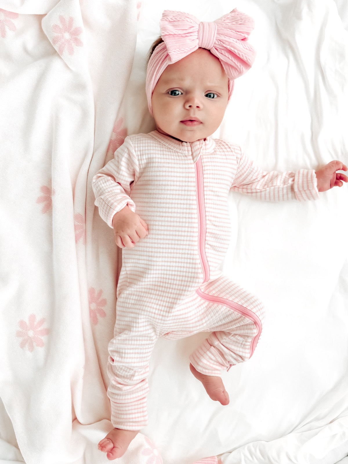 Baby girl in pink striped onesie and oversized bow, lying on a soft floral blanket.
