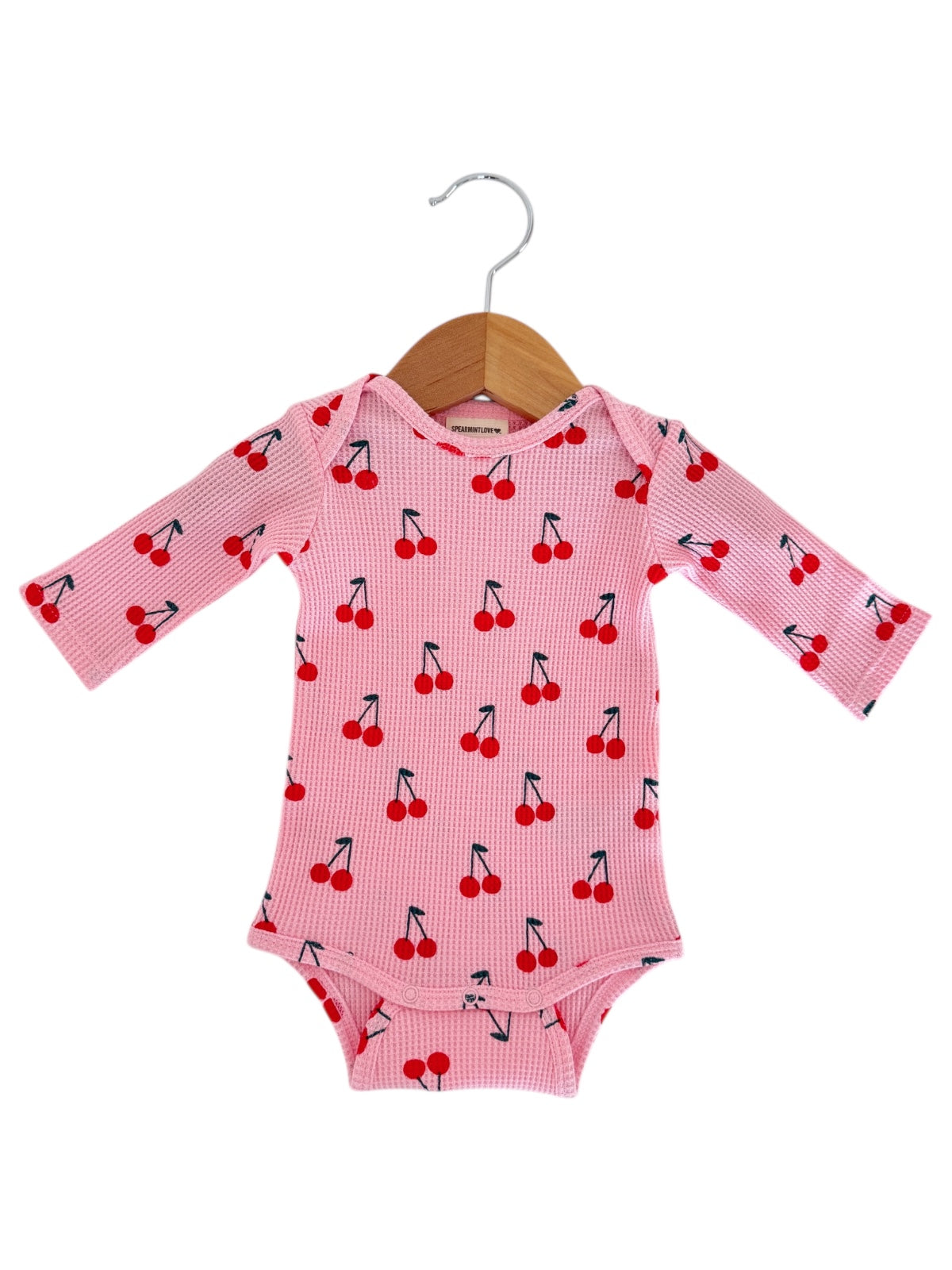 Pink long-sleeve baby bodysuit with red cherry print, displayed on a wooden hanger.