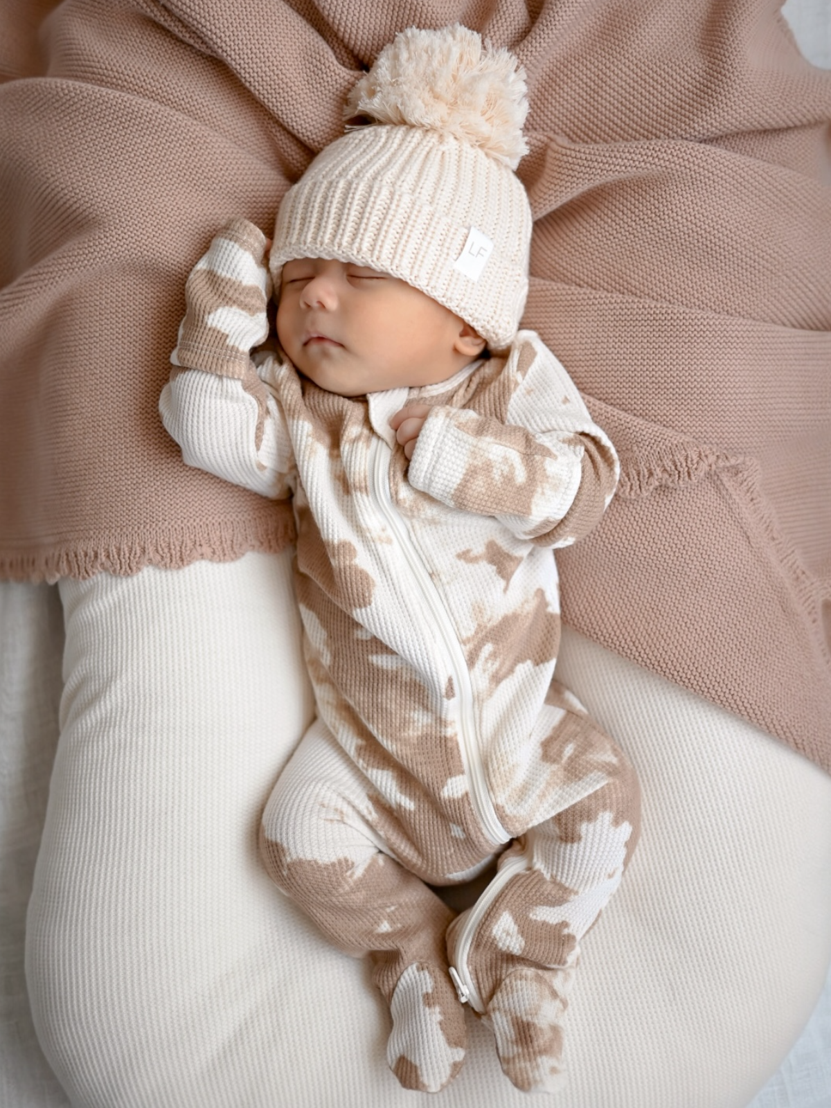Newborn sleeping peacefully in cozy outfit and knitted hat on a soft blanket.