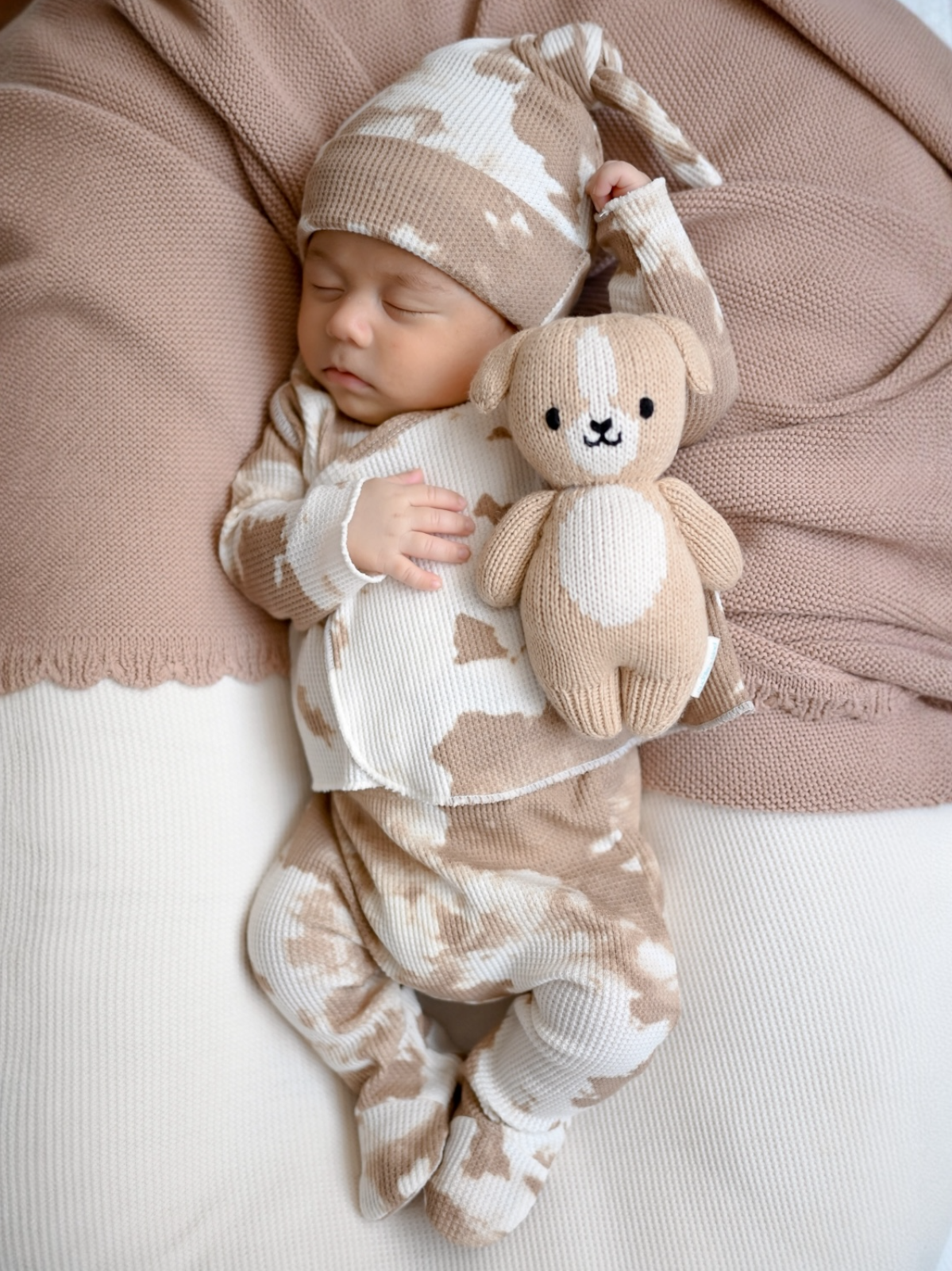 Sleeping baby in beige-patterned outfit holds a soft toy on a neutral background. Cozy and peaceful scene.