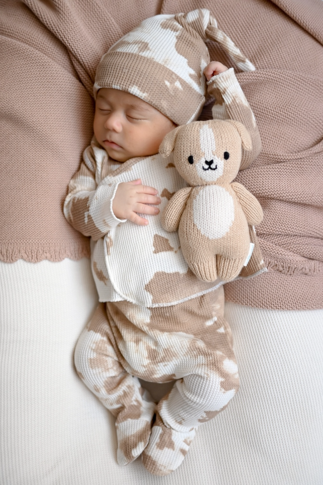 Sleeping baby in beige-patterned outfit holds a soft toy on a neutral background. Cozy and peaceful scene.
