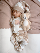 Sleeping baby in beige-patterned outfit holds a soft toy on a neutral background. Cozy and peaceful scene.