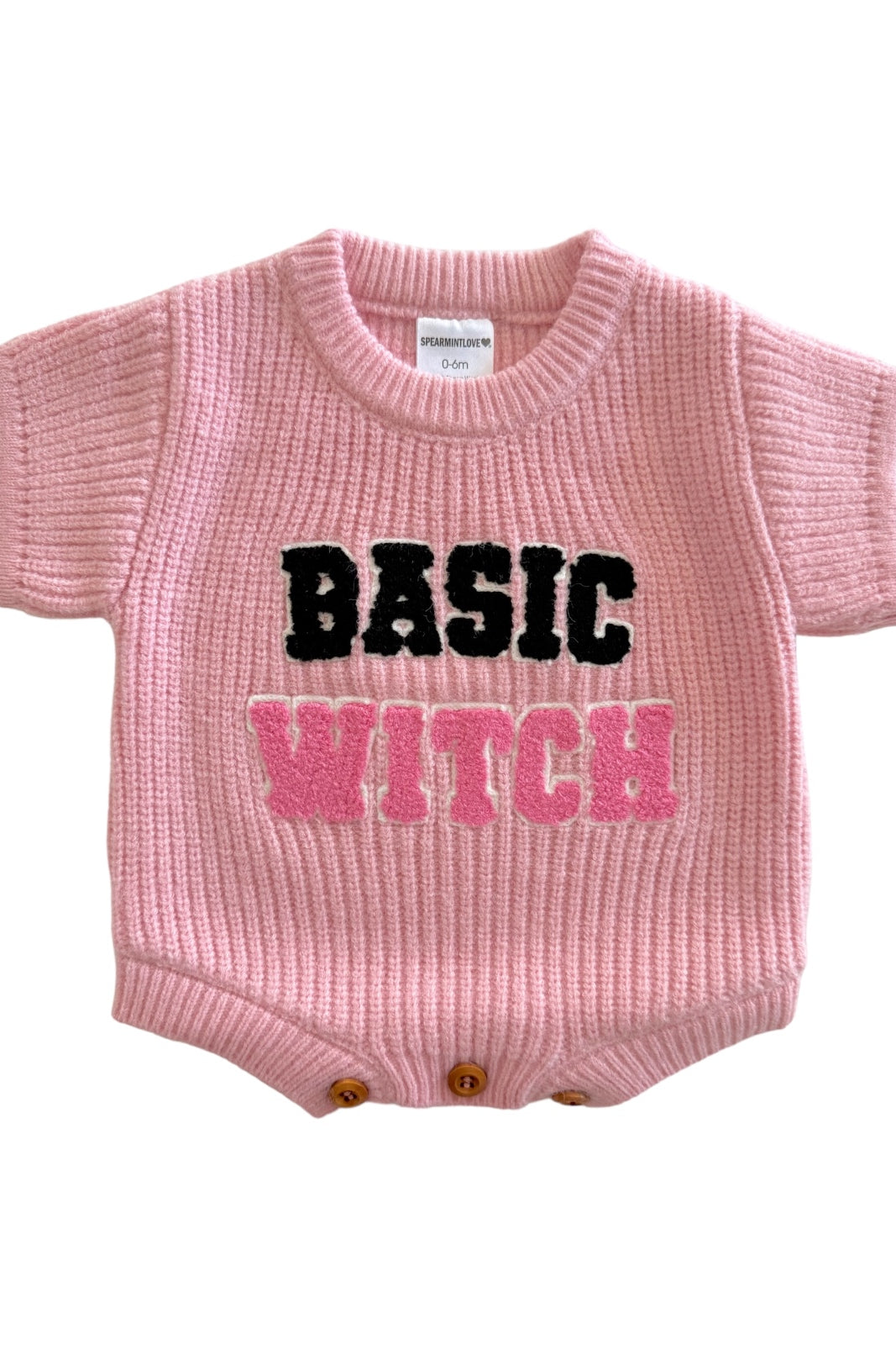 Pink knitted baby onesie with "BASIC WITCH" in bold, colorful letters.