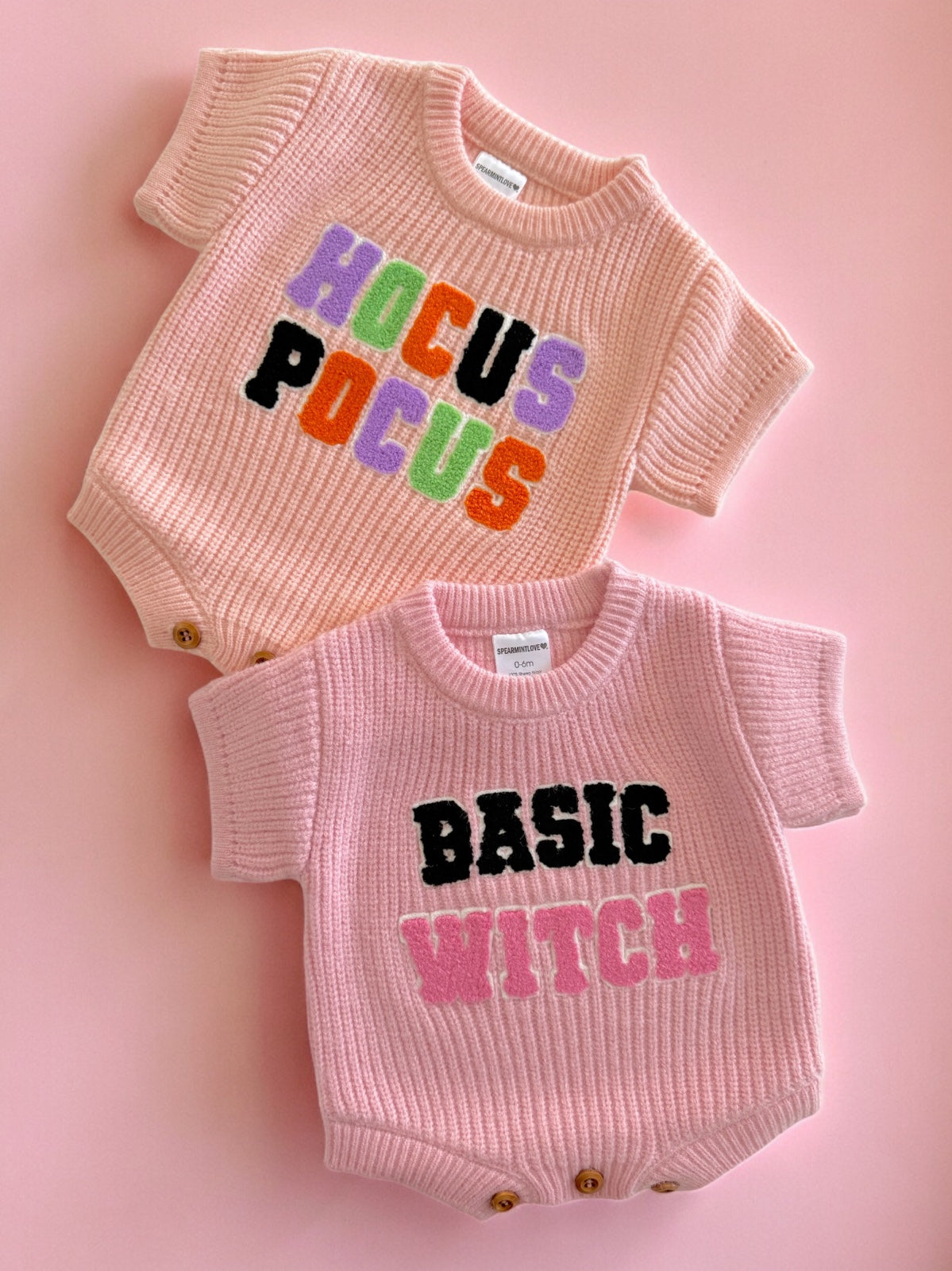 Two pink baby outfits with graphic text: "Hocus Pocus" on top and "Basic Witch" on the bottom, set against a pink background.