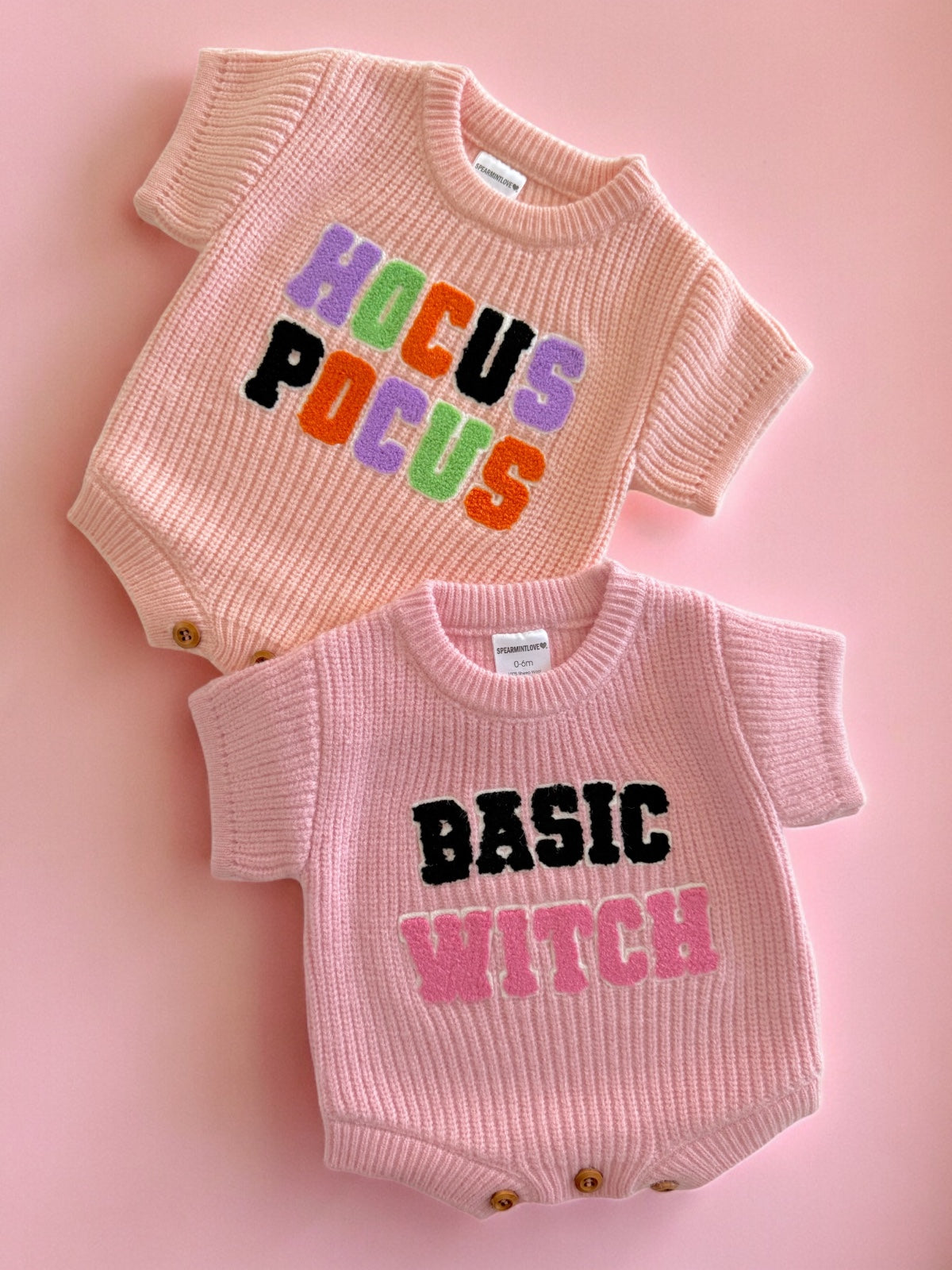 Two pink baby outfits with graphic text: "Hocus Pocus" on top and "Basic Witch" on the bottom, set against a pink background.