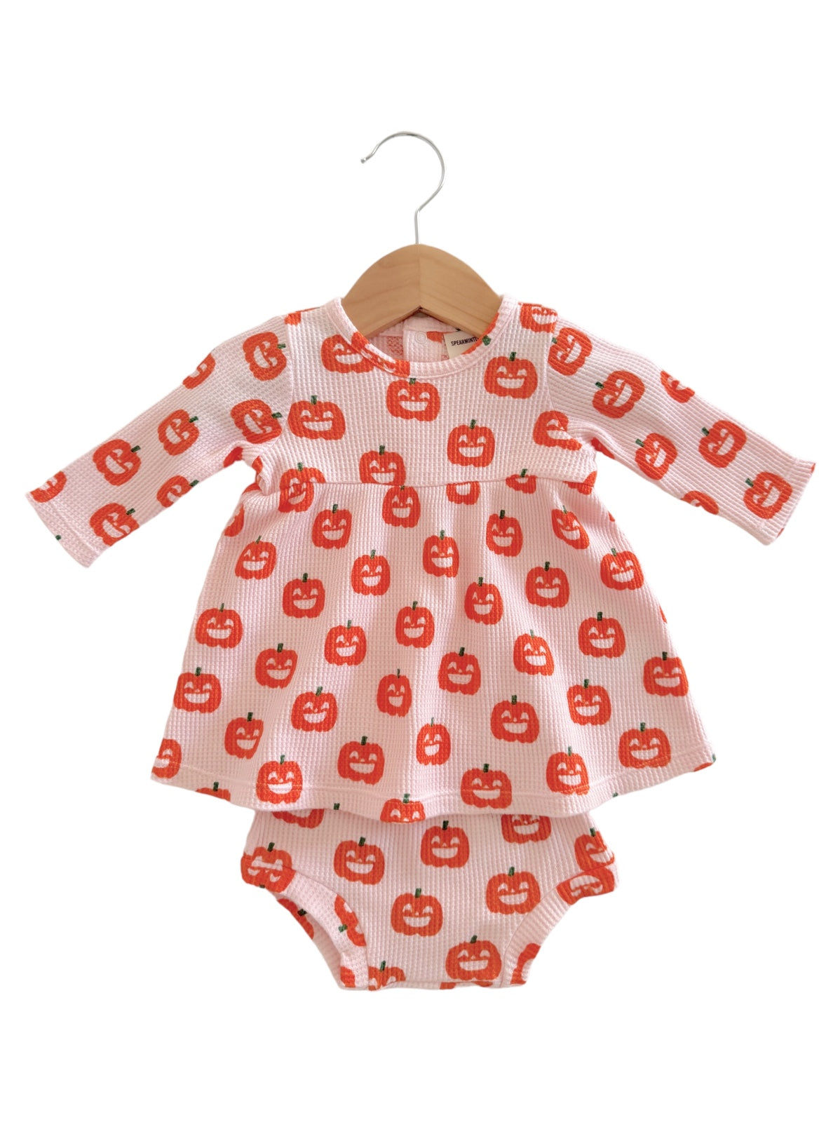 Baby dress with long sleeves, featuring a pumpkin pattern, hanging on a wooden hanger.