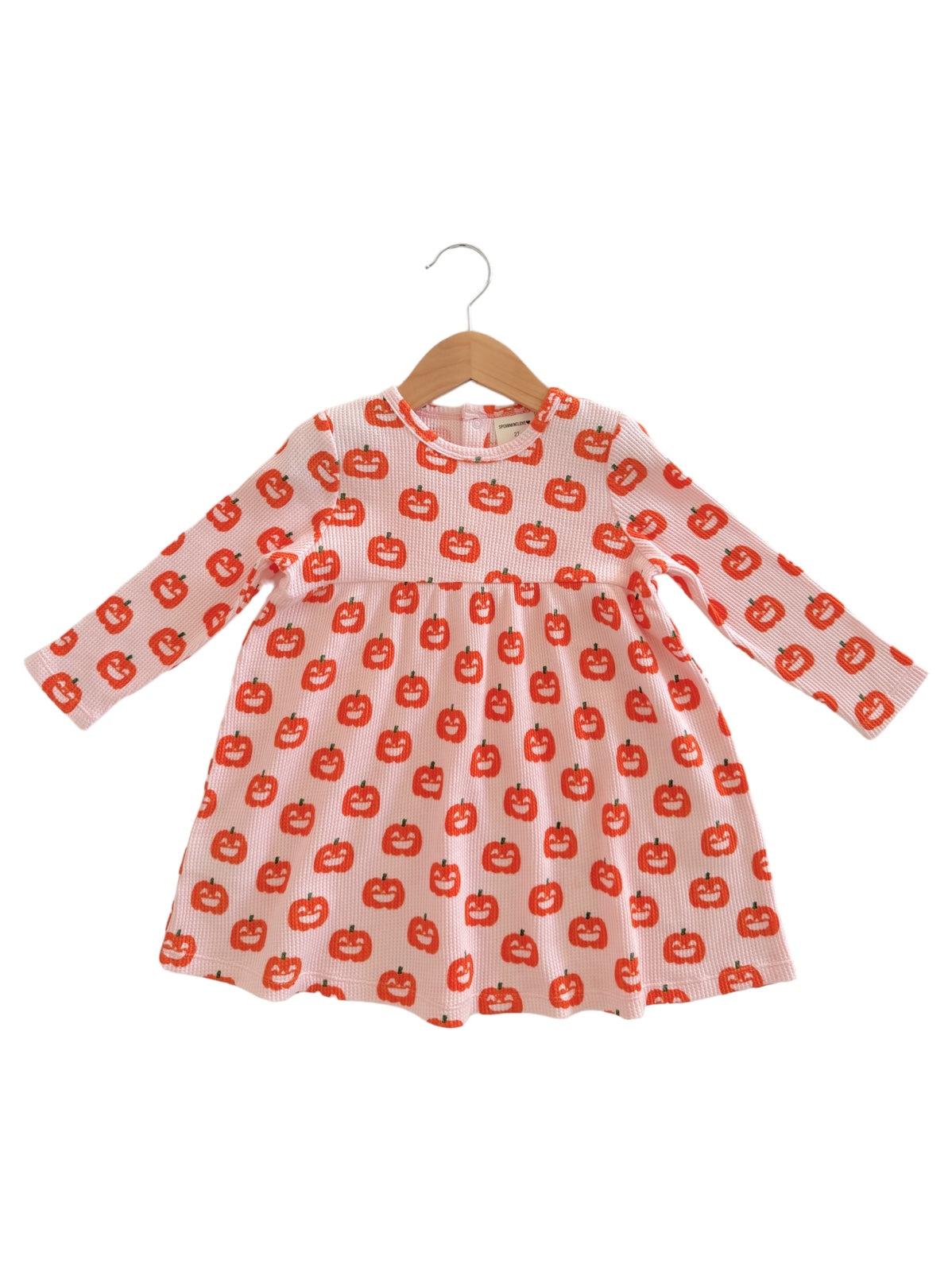 Children's dress with long sleeves featuring a playful pumpkin pattern on a light orange background.