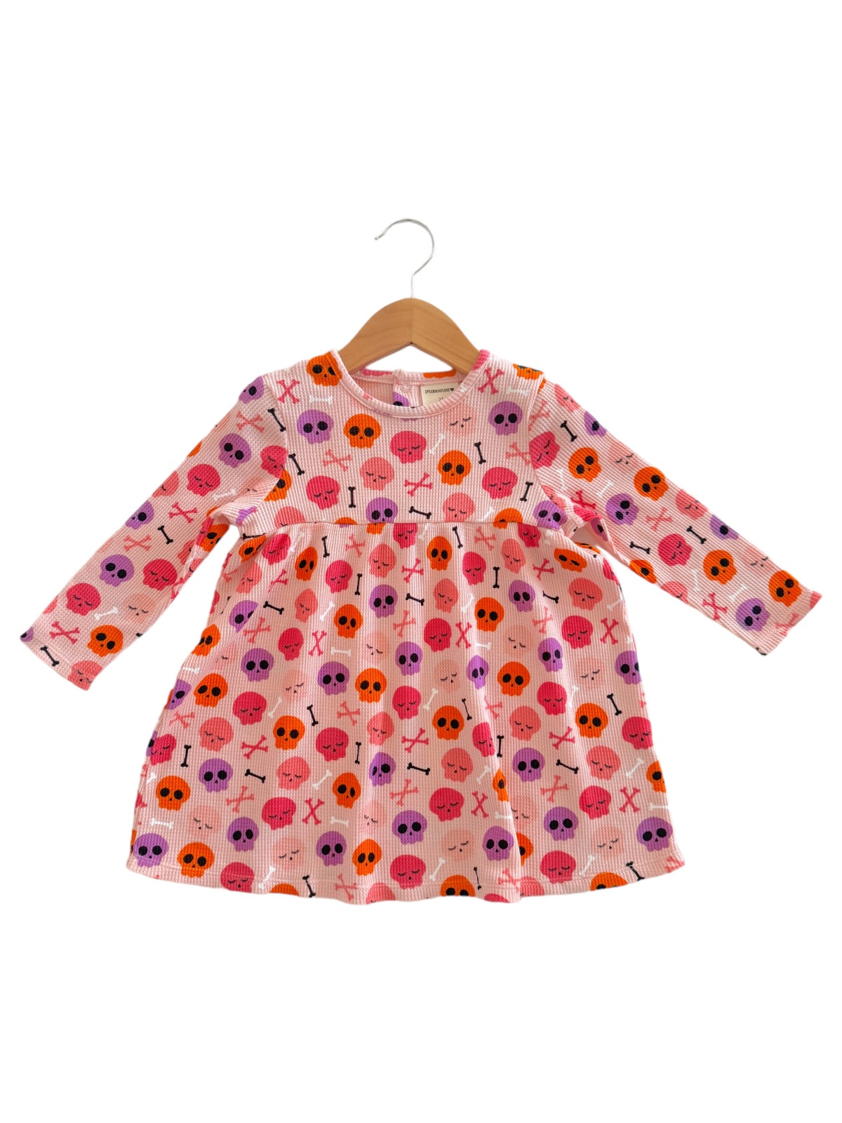 Pink long-sleeve dress with colorful skull and crossbones pattern on hanger. Ideal for kids' Halloween apparel.