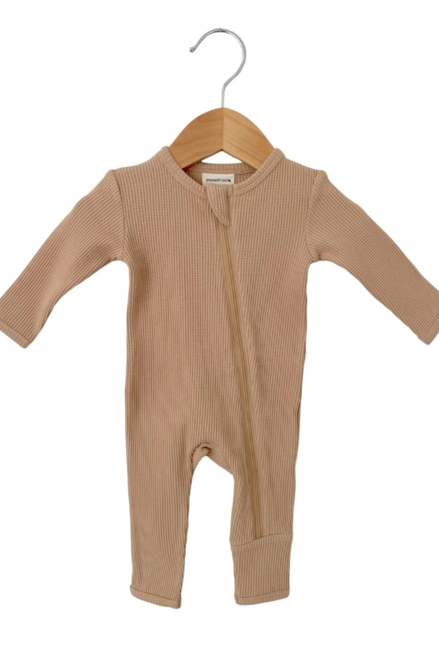 Beige ribbed infant jumpsuit hanging on a wooden hanger against a white background.
