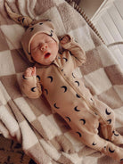 Baby in a cozy, moon-patterned onesie sleeps on a soft checkered blanket.