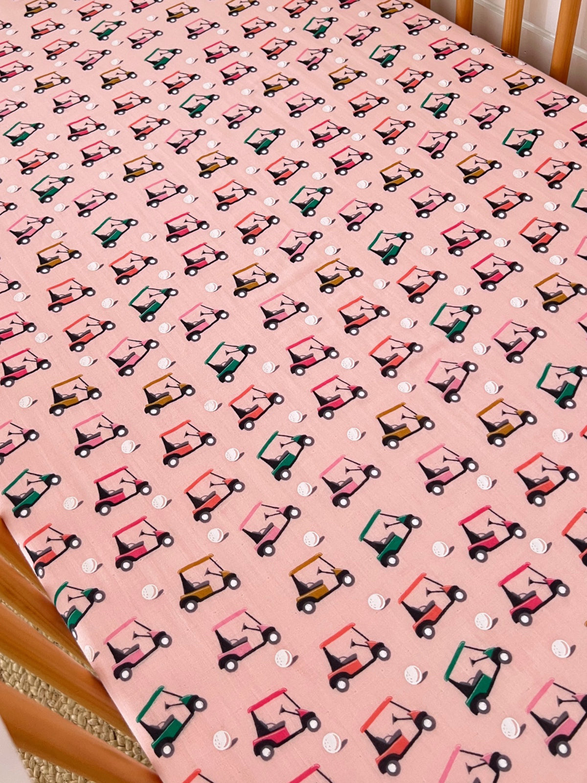 Pink fabric with a repeated pattern of colorful golf carts and small white golf balls. Ideal for playful decor.