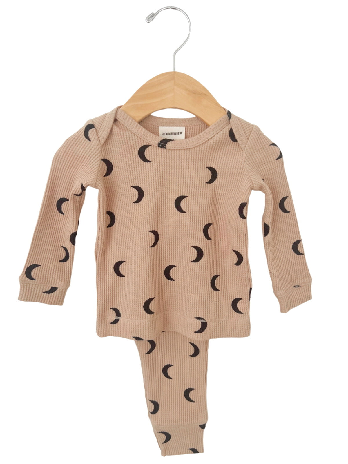 Beige children's pajama set with black crescent moon patterns, hanging on a wooden hanger.