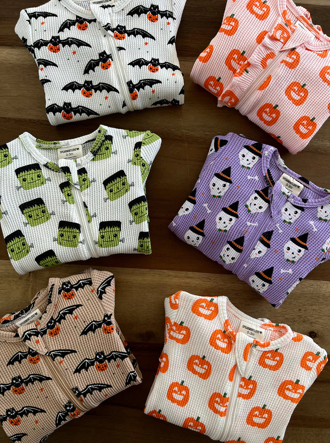 Assorted children’s pajamas featuring Halloween designs like bats, pumpkins, and ghosts on a wooden surface.