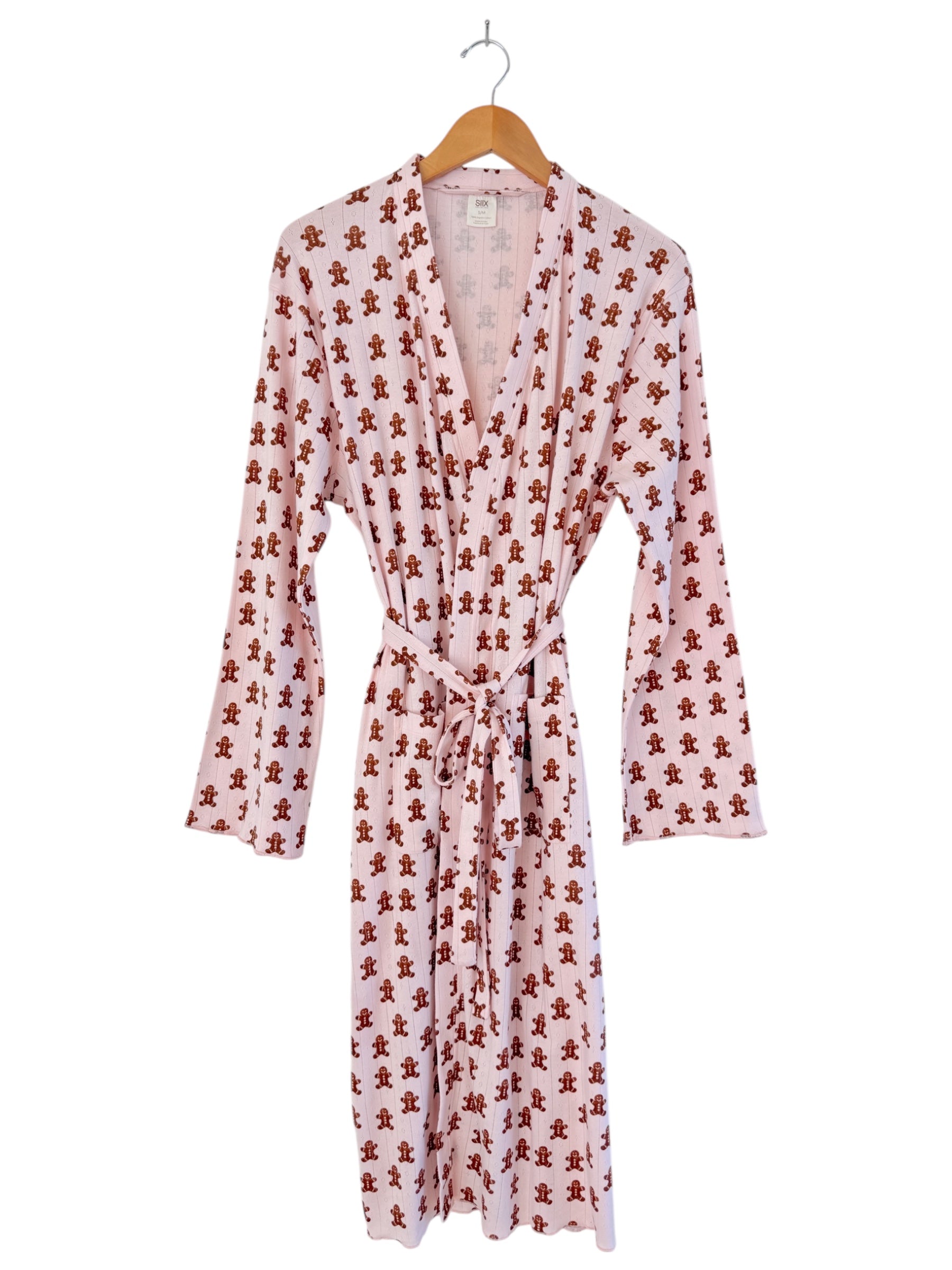 Pink robe with gingerbread man print, featuring long sleeves and a tie belt, hanging on a wooden hanger.
