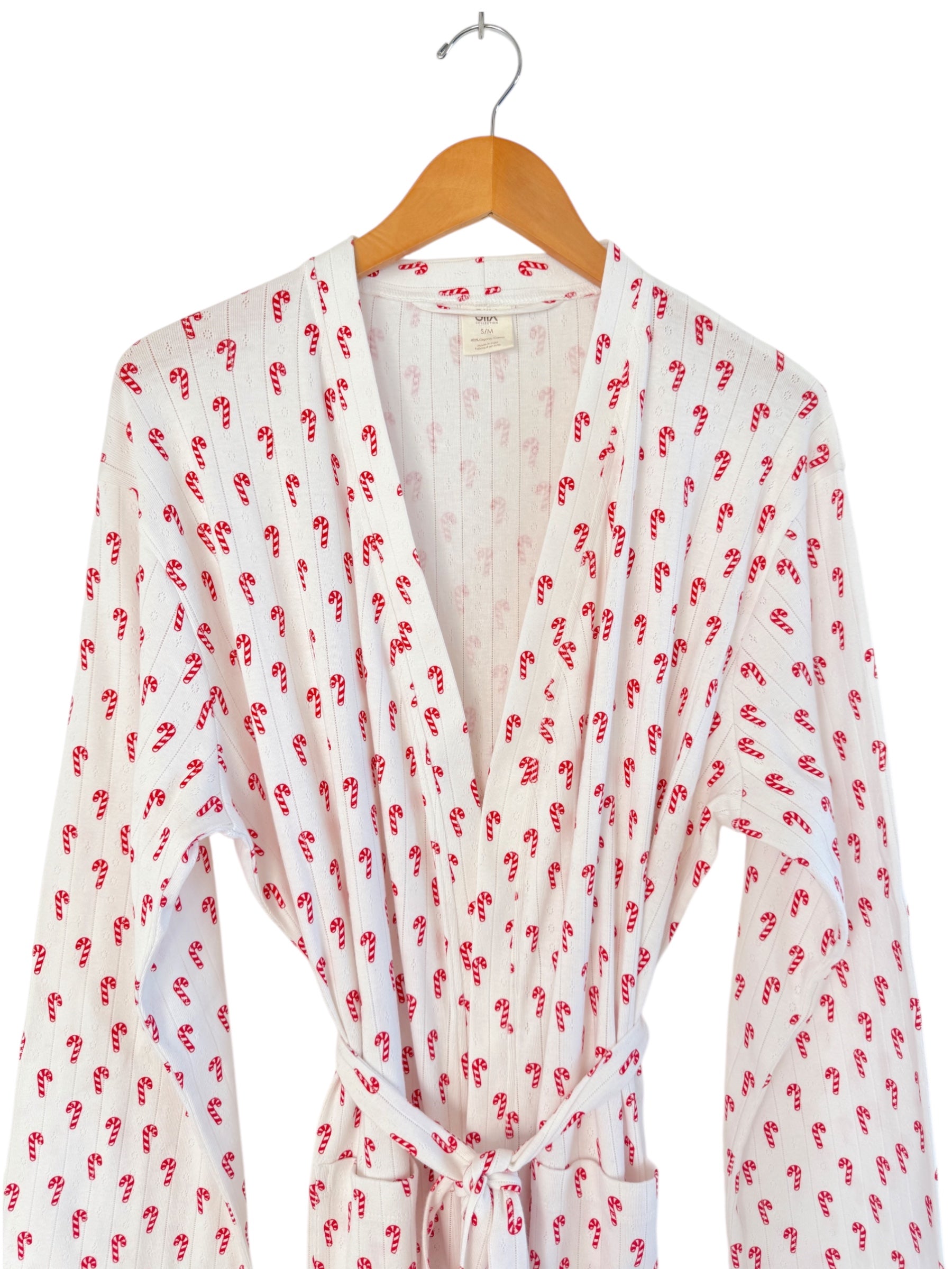White robe with red candy cane pattern, hanging on a wooden hanger against a neutral background.