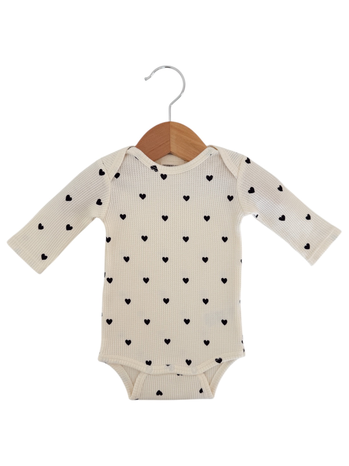 Baby onesie with long sleeves, cream color, featuring a pattern of small black hearts.