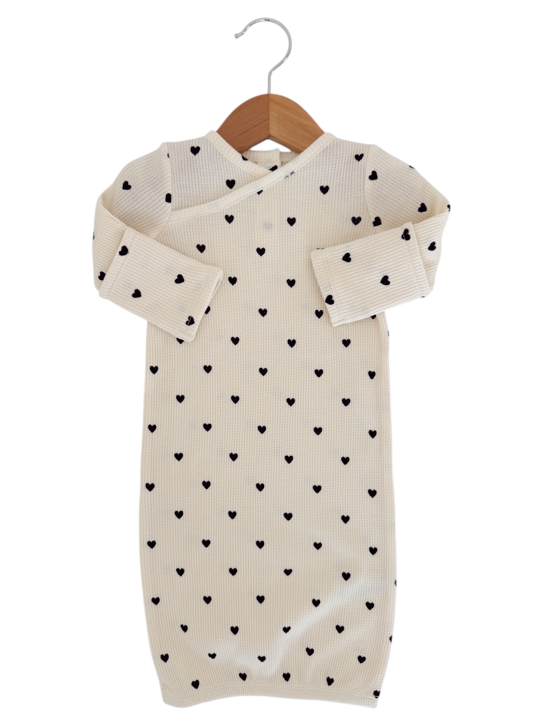 Cream-colored baby gown with black heart patterns, hung on a wooden hanger.