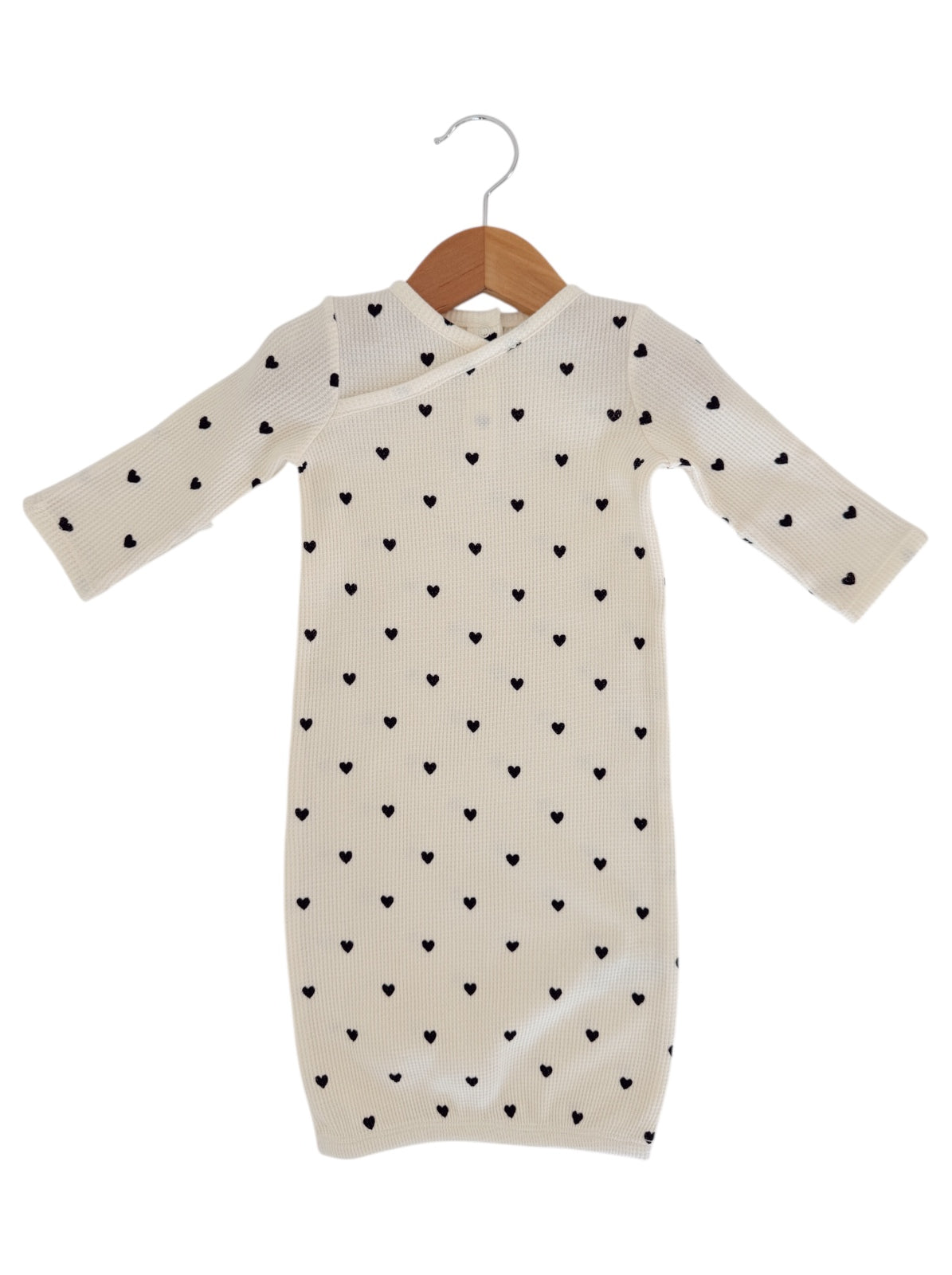 Cream dress with long sleeves and black heart patterns, hanging on a wooden hanger.