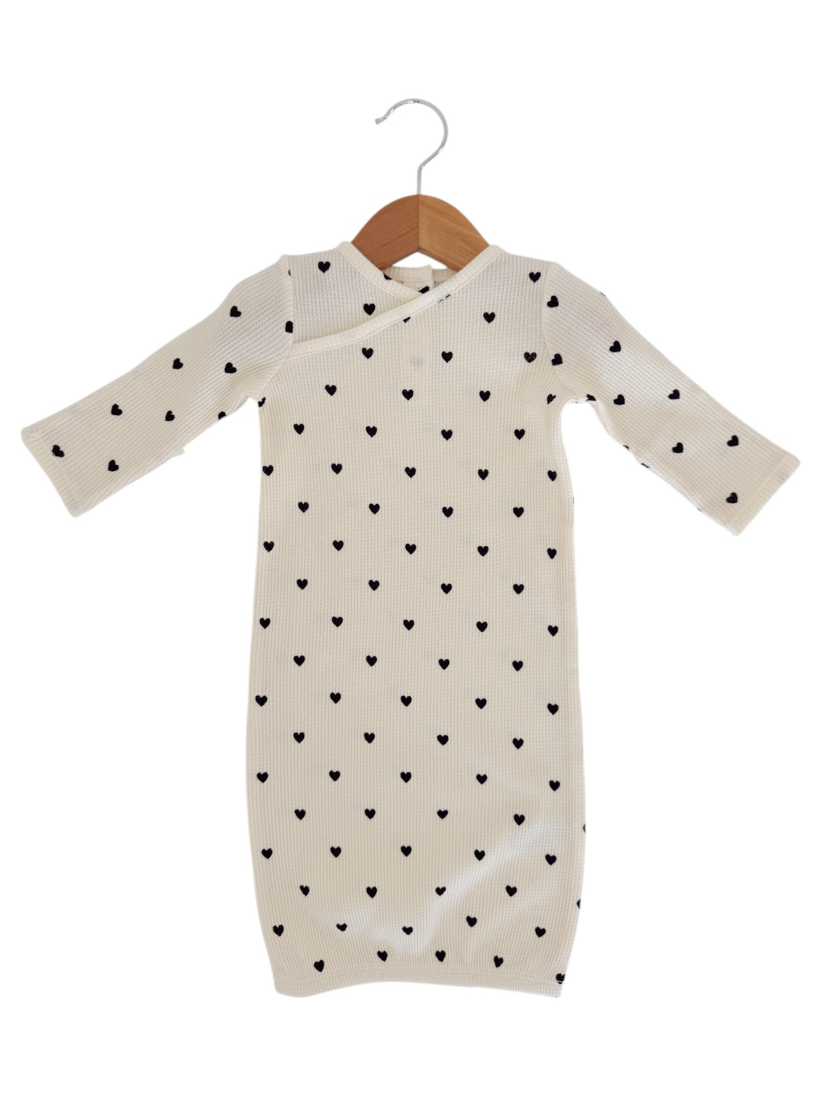 Cream dress with long sleeves and black heart patterns, hanging on a wooden hanger.