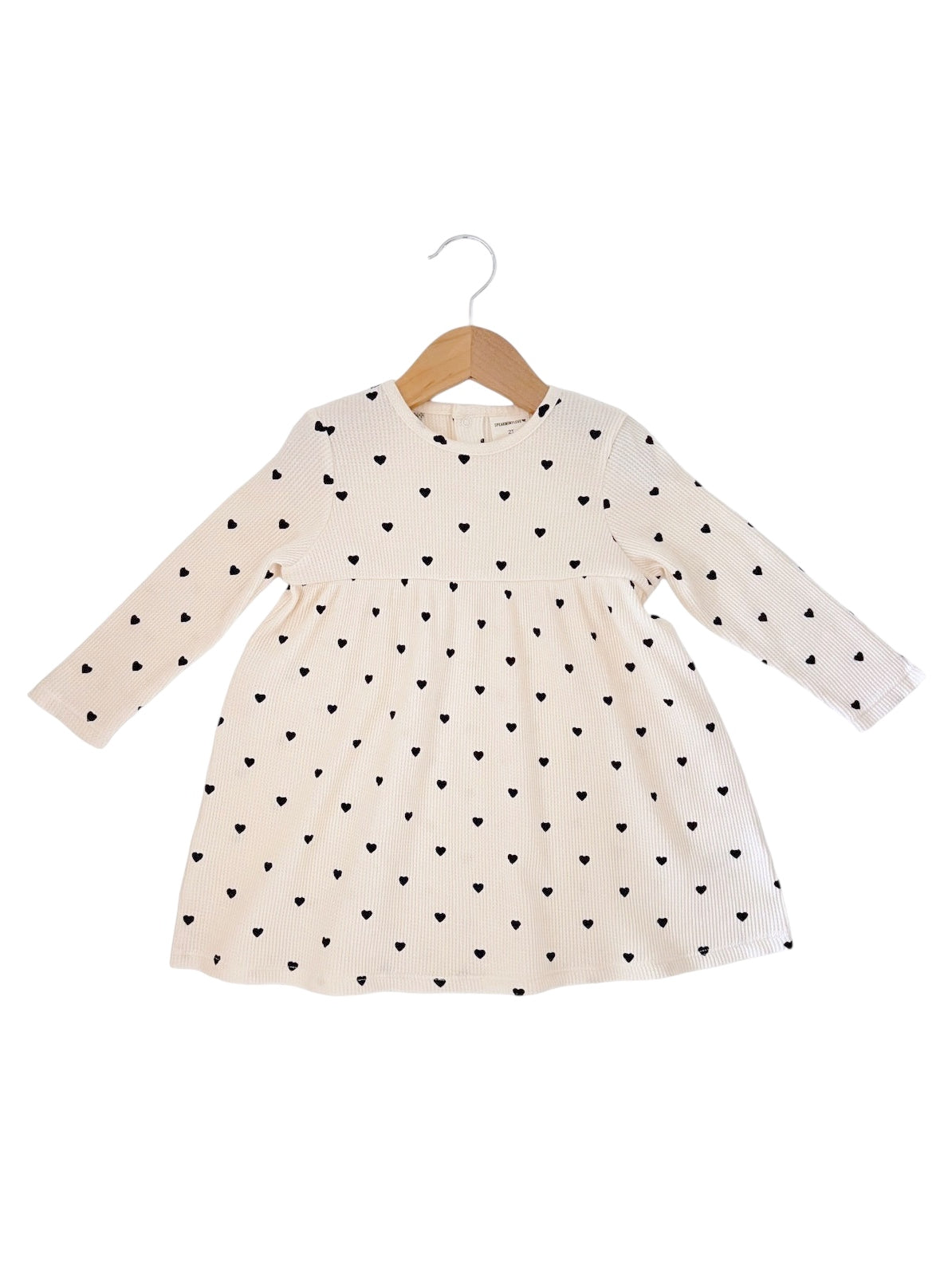 Cream dress with black heart pattern, long sleeves, and flared skirt, hanging on a wooden hanger.